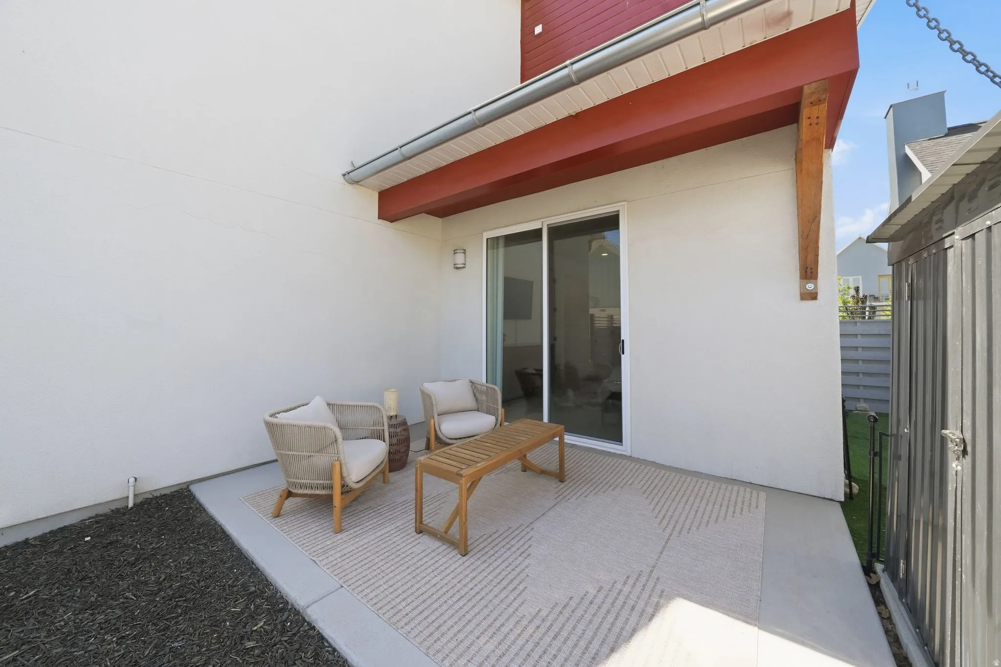 Outdoor patio featuring a stucco exterior, sliding glass doors, a modern wall sconce, and an exposed wood beam detail