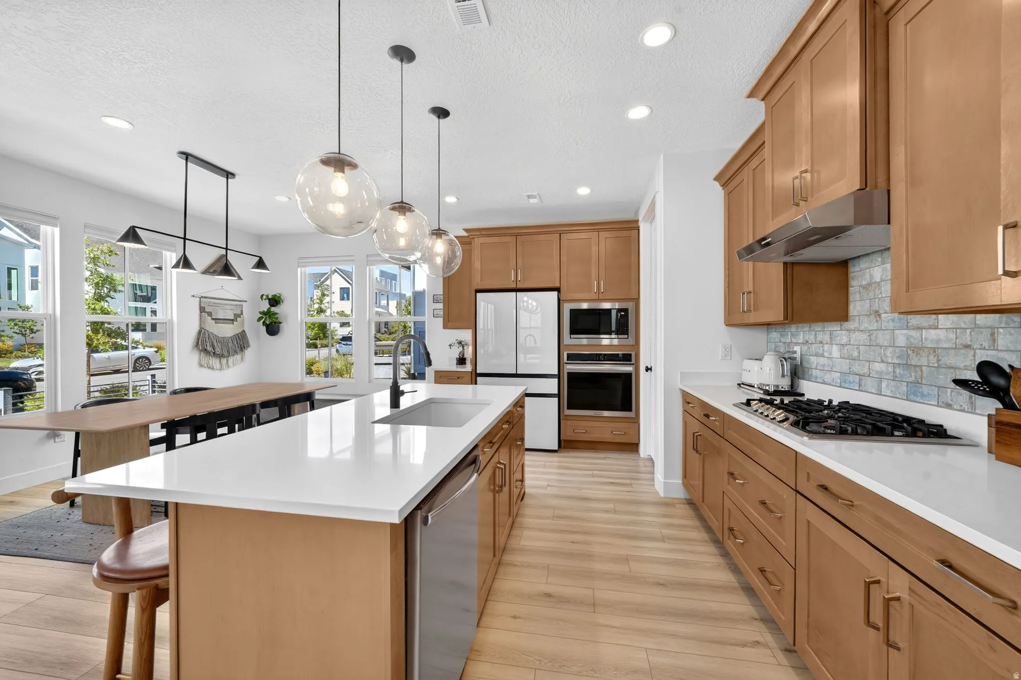 Kitchen featuring light wood-finish cabinetry and flooring, white countertops, and a subway tile backsplash