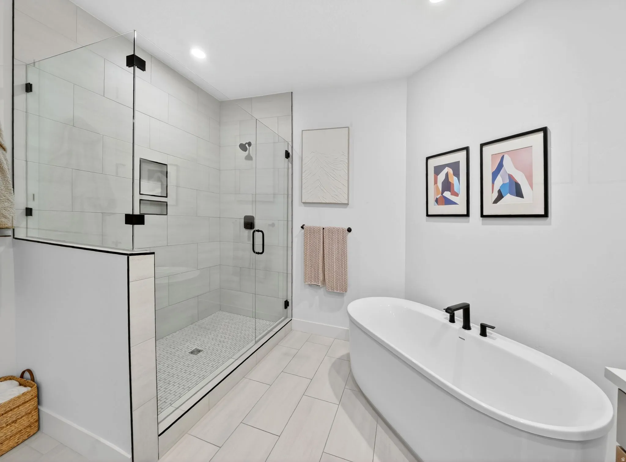 Sleek bathroom featuring a spacious glass-enclosed shower with subway tile surround and integrated shelving, a freestanding oval soaking tub with matte black fixtures, and light-toned wood-finish flooring