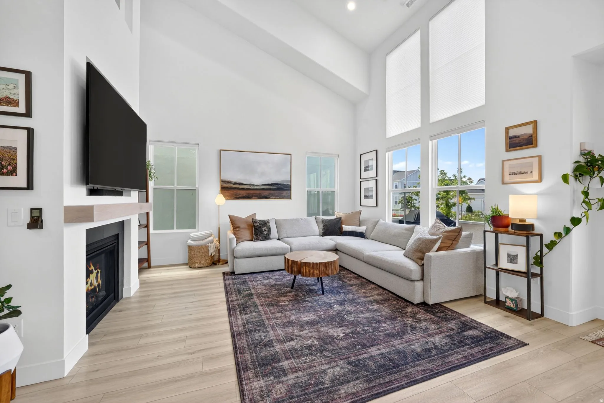 Living area featuring a modern fireplace with a light wood-finish mantel, wood-finish flooring, high ceilings, and large windows with transom panels