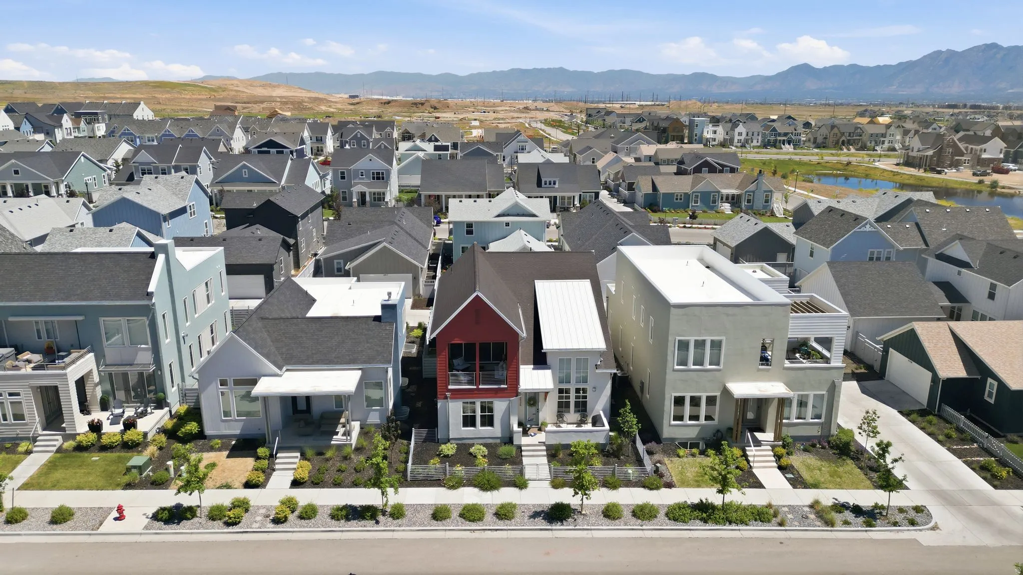 Modern residential community featuring diverse architectural styles, a visible pond, and mountain backdrop