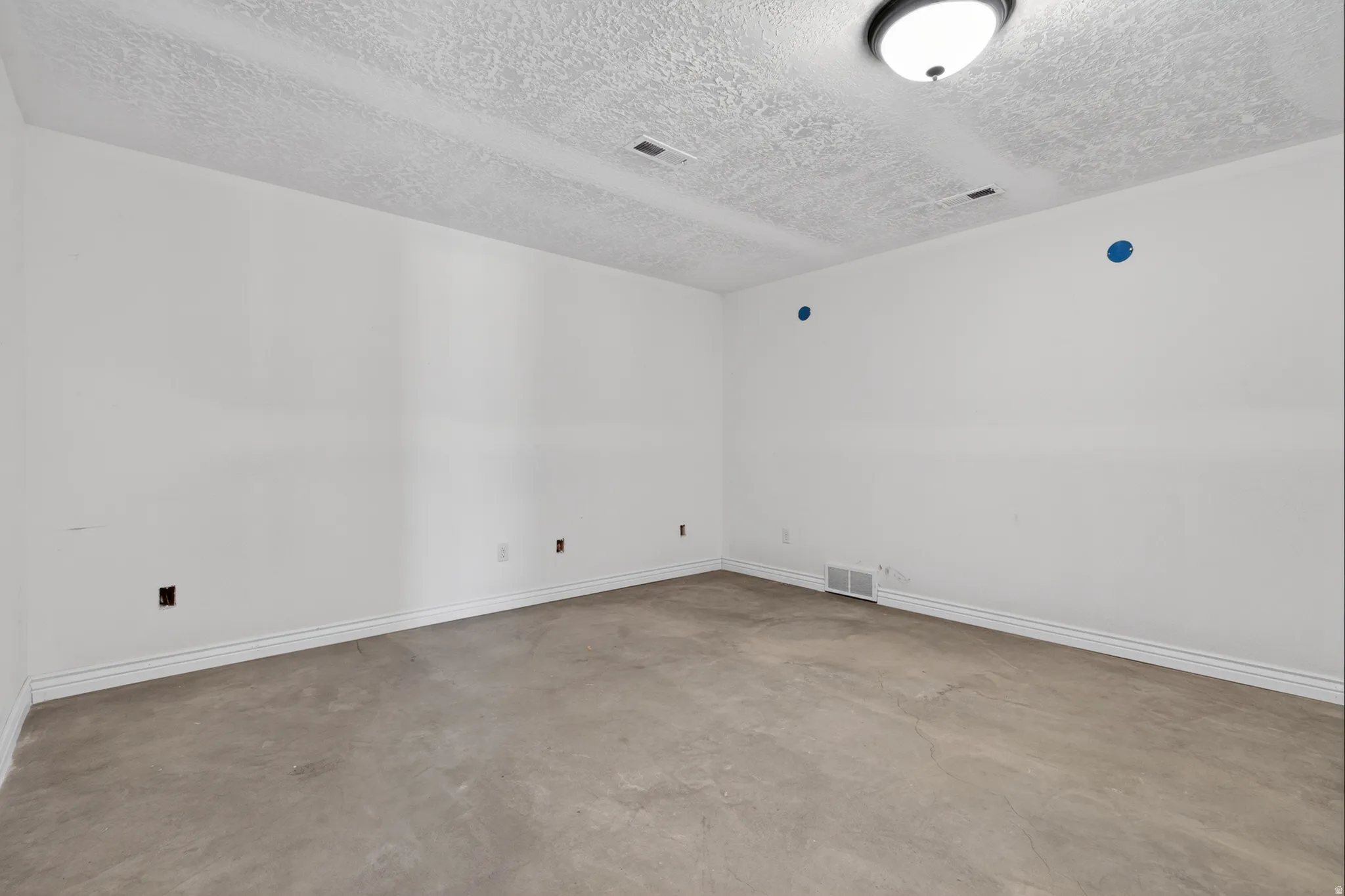 Spacious room featuring white painted walls, textured ceiling, and concrete flooring