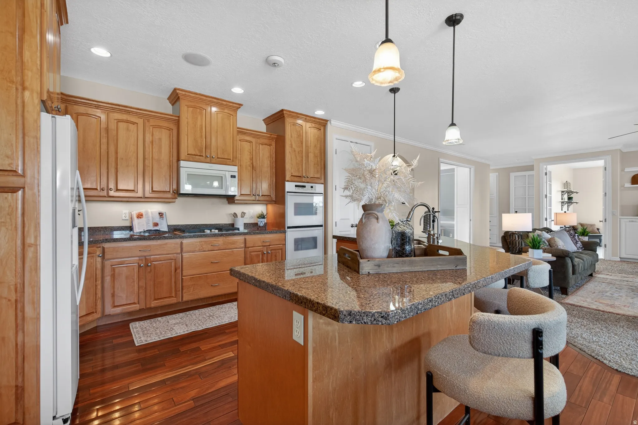 Kitchen featuring wood cabinetry, granite countertops, built-in double ovens, and a central island with sink
