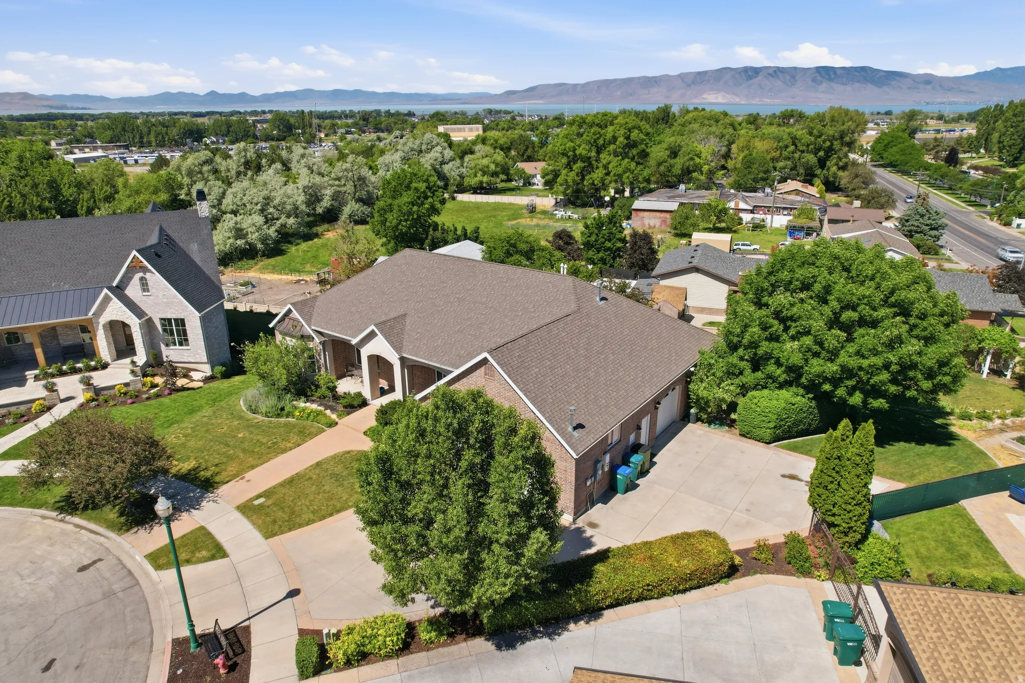 Brick exterior residence with an attached garage, a paved driveway, and mature landscaping