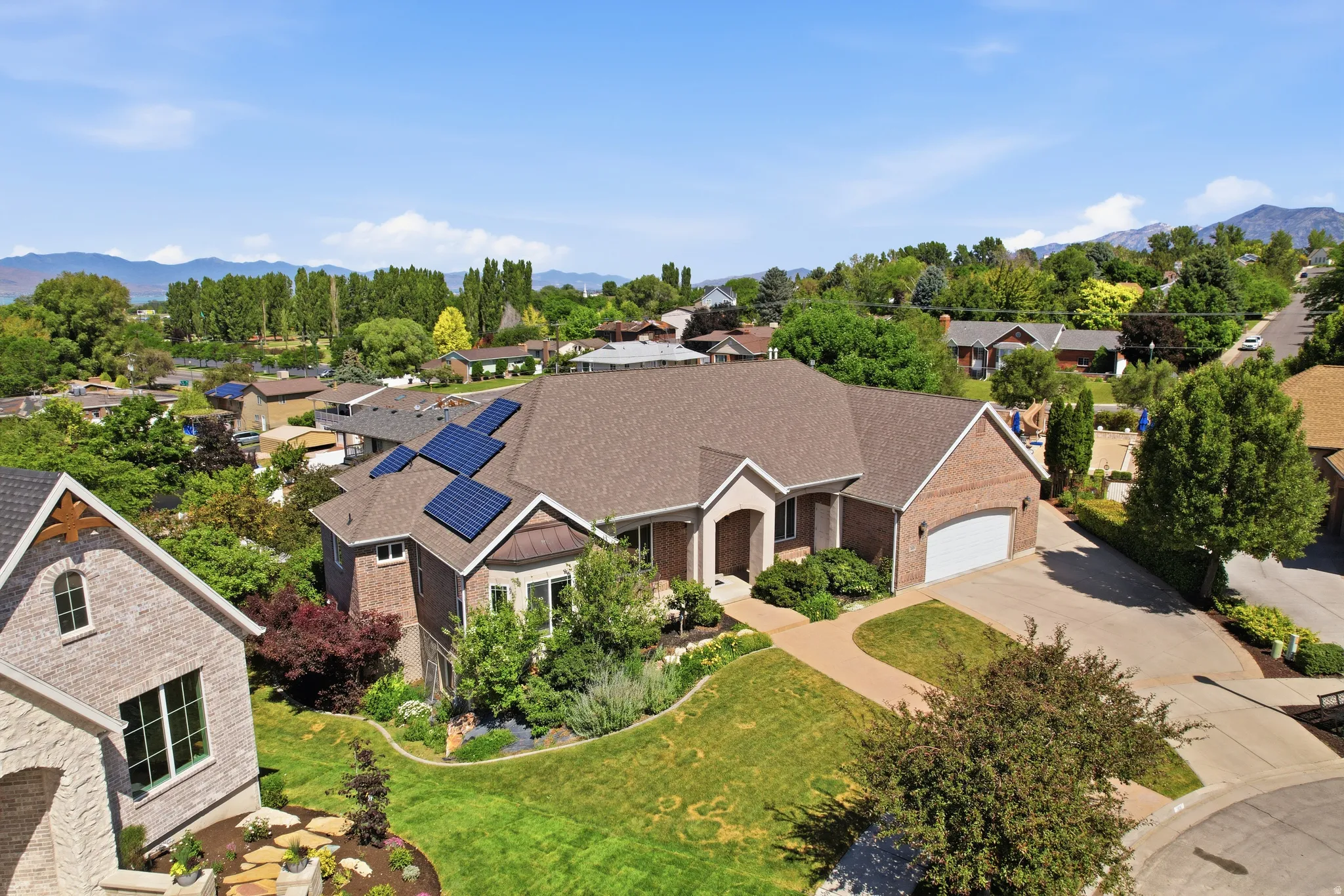 Brick exterior residence featuring a multi-panel solar array, a two-car garage, and a curved paved driveway