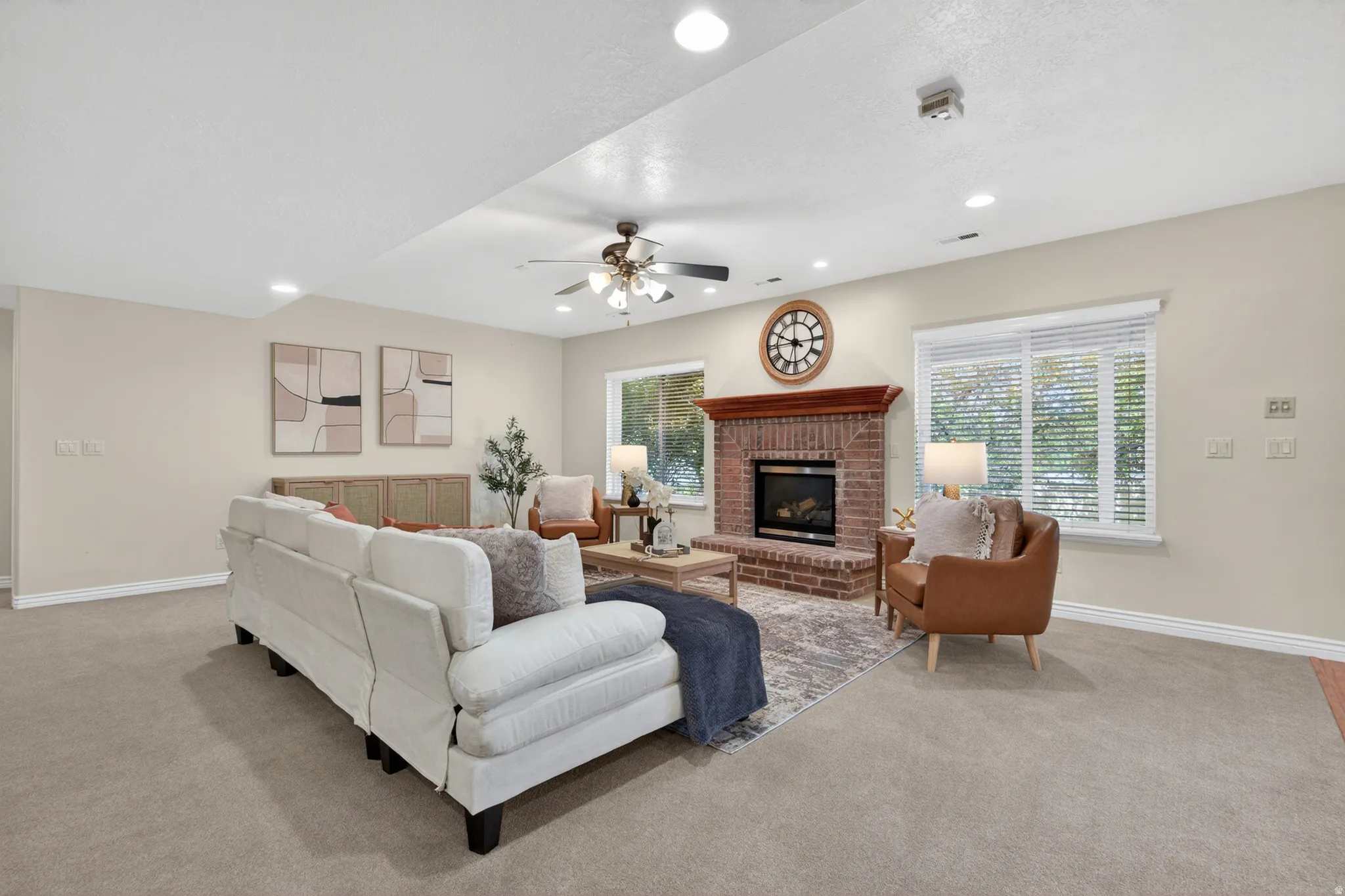 Spacious living area featuring a brick fireplace with a wood mantel, recessed lighting, and multiple windows with blinds