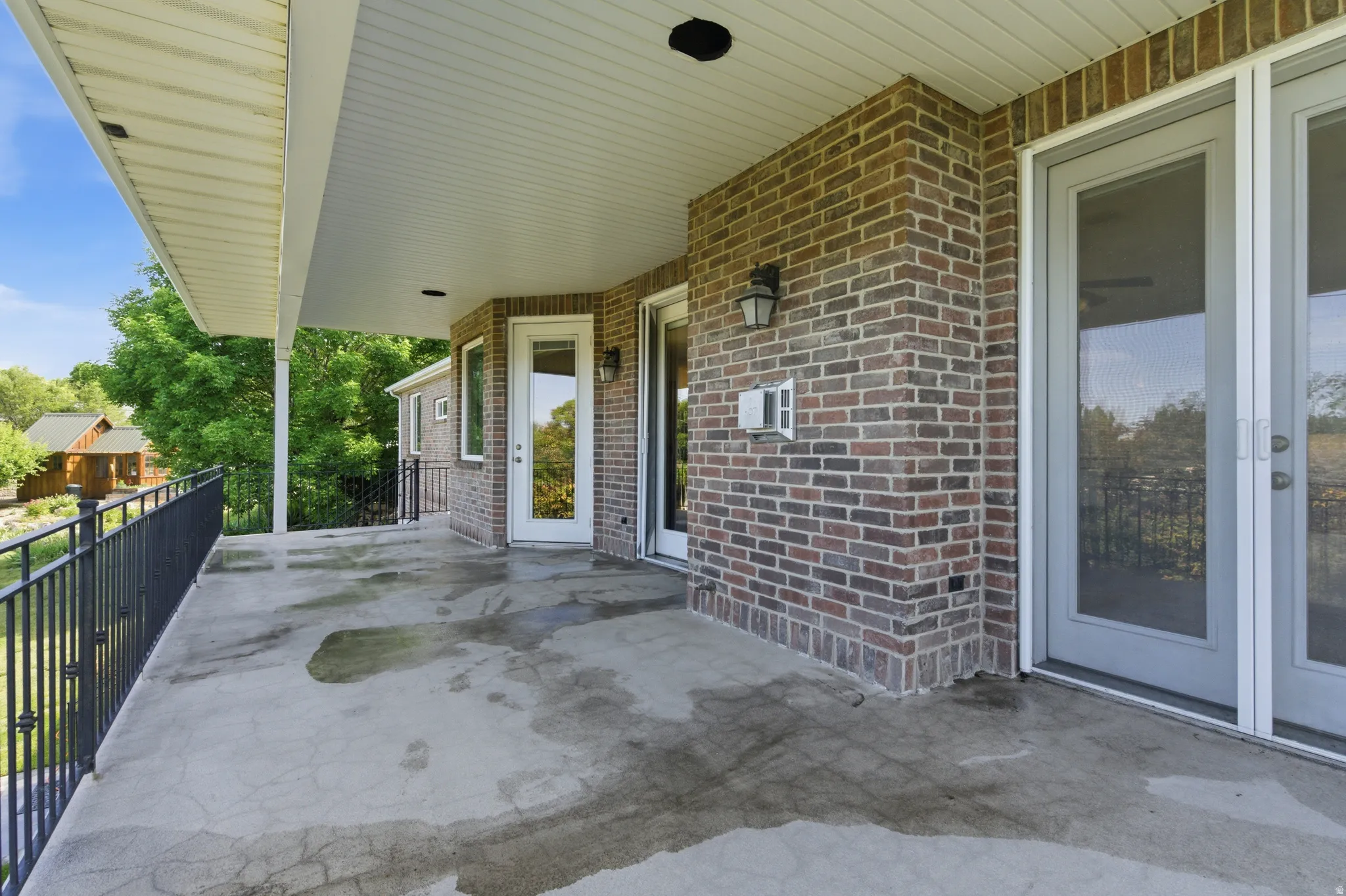 Expansive covered patio featuring a concrete surface, black iron railings, multiple exterior doors, recessed lighting, and brick exterior walls