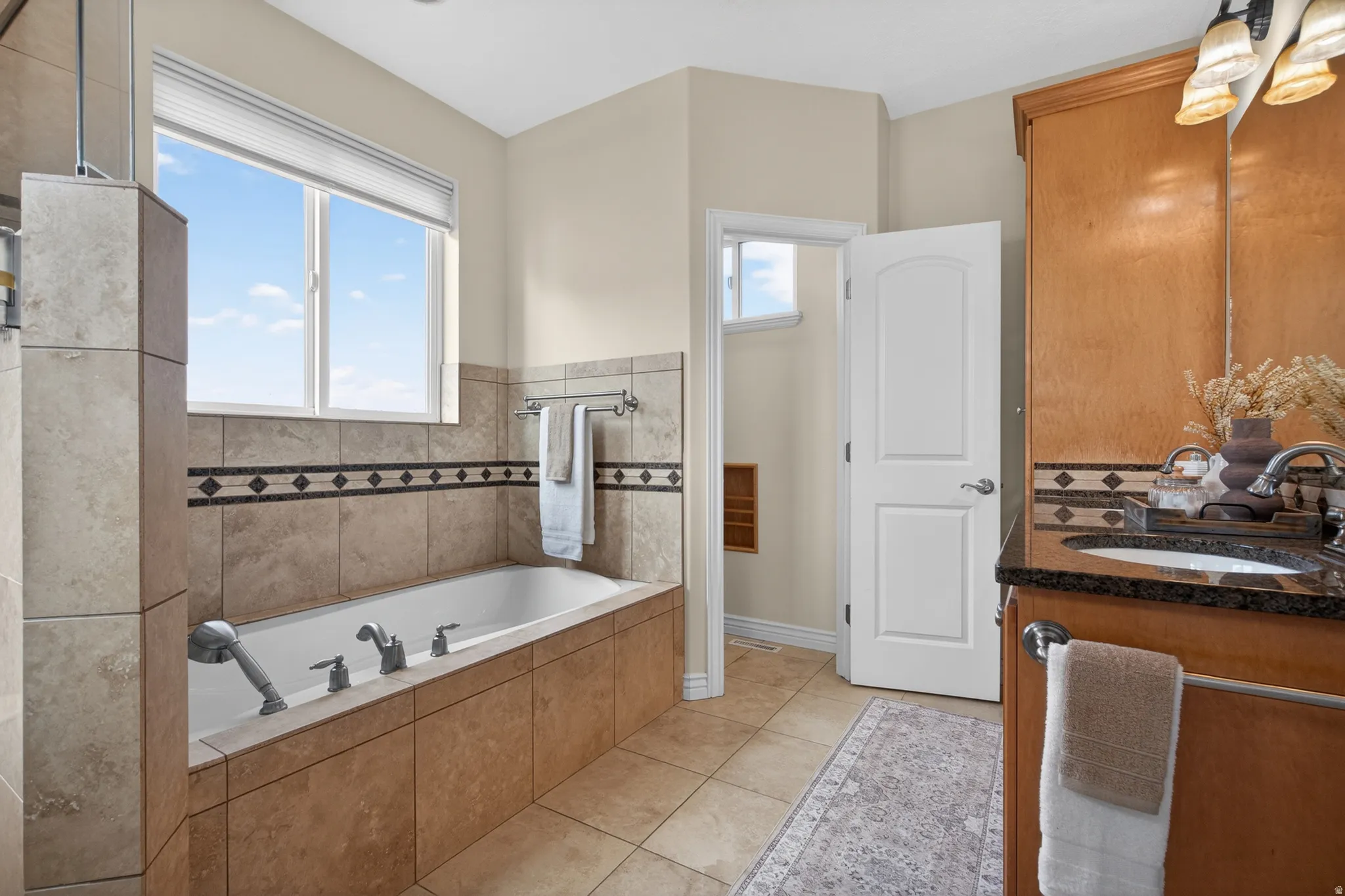 Soaking tub with a tile surround and decorative accent band, featuring a window with privacy blinds
