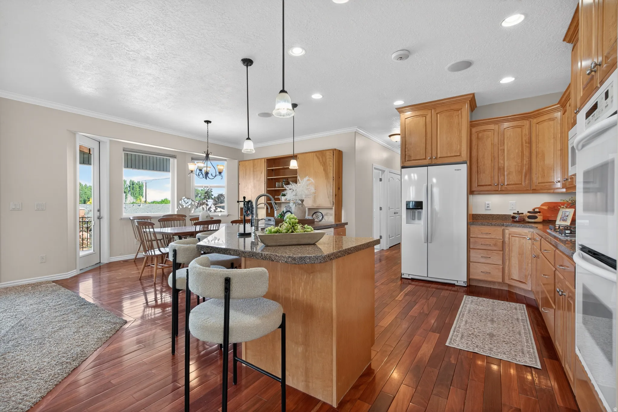 Kitchen featuring wood-finish flooring, light wood cabinetry, granite countertops, an island with pendant lighting, and built-in double ovens