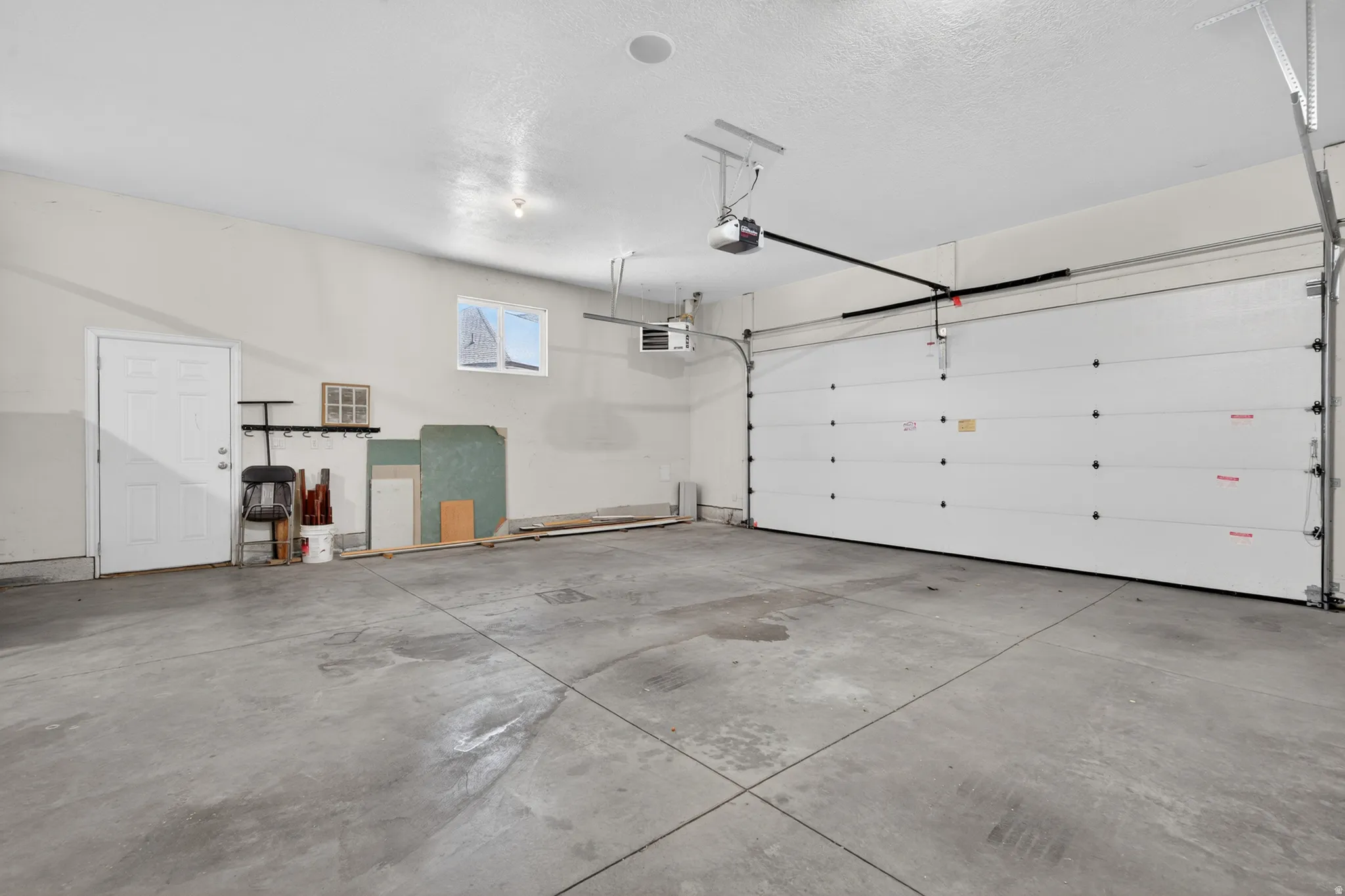 Spacious garage featuring a concrete floor, overhead lighting, an automatic garage door opener, a side entry door, and a window for natural light