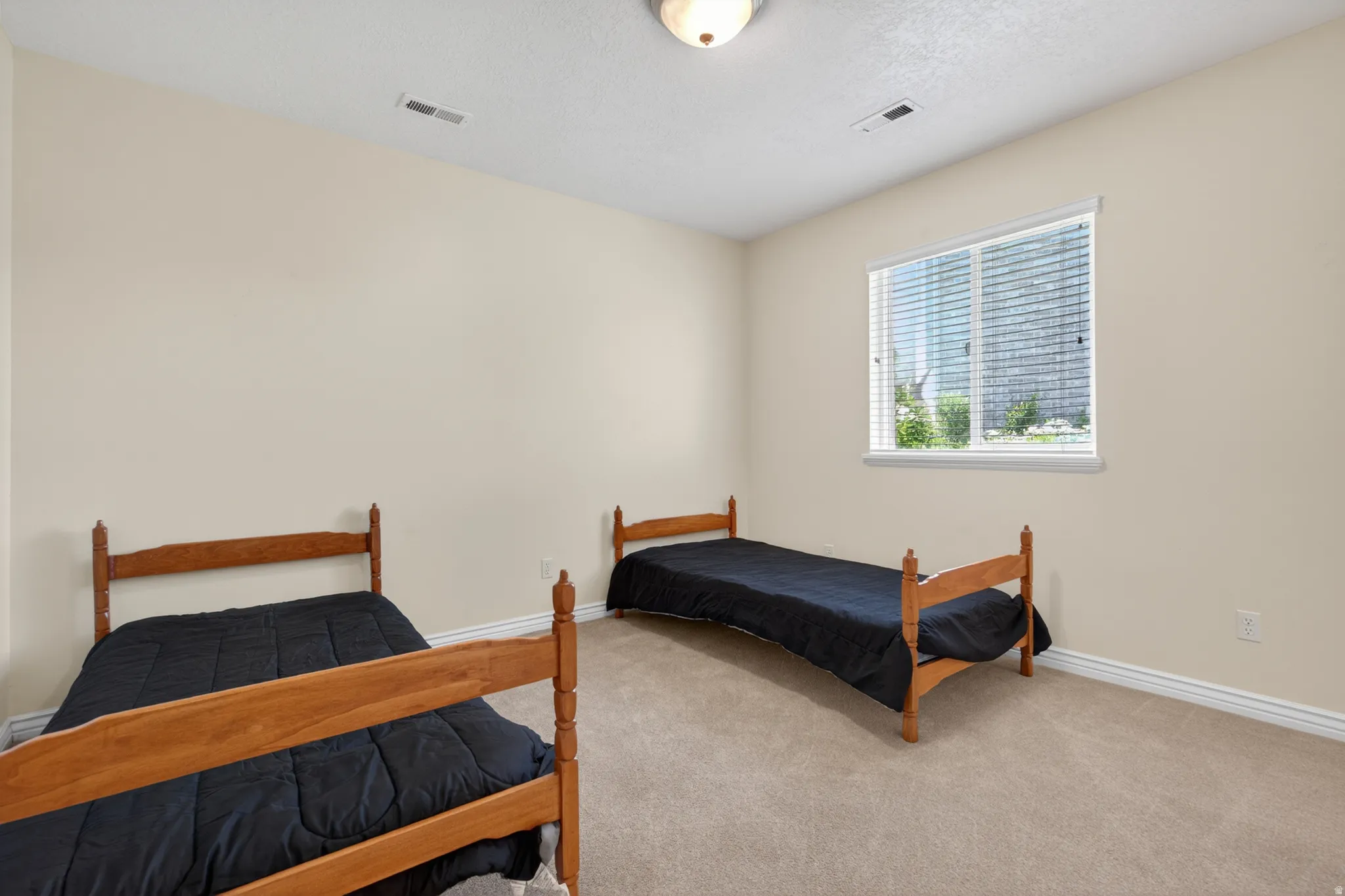 Carpeted room featuring neutral wall tones, a single window with blinds, and a ceiling-mounted light fixture