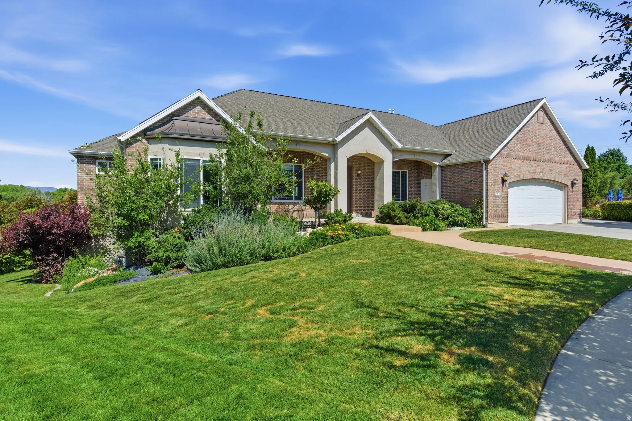Brick and stucco exterior featuring a curved concrete driveway, an arched entry, a two-car garage, and established landscaping