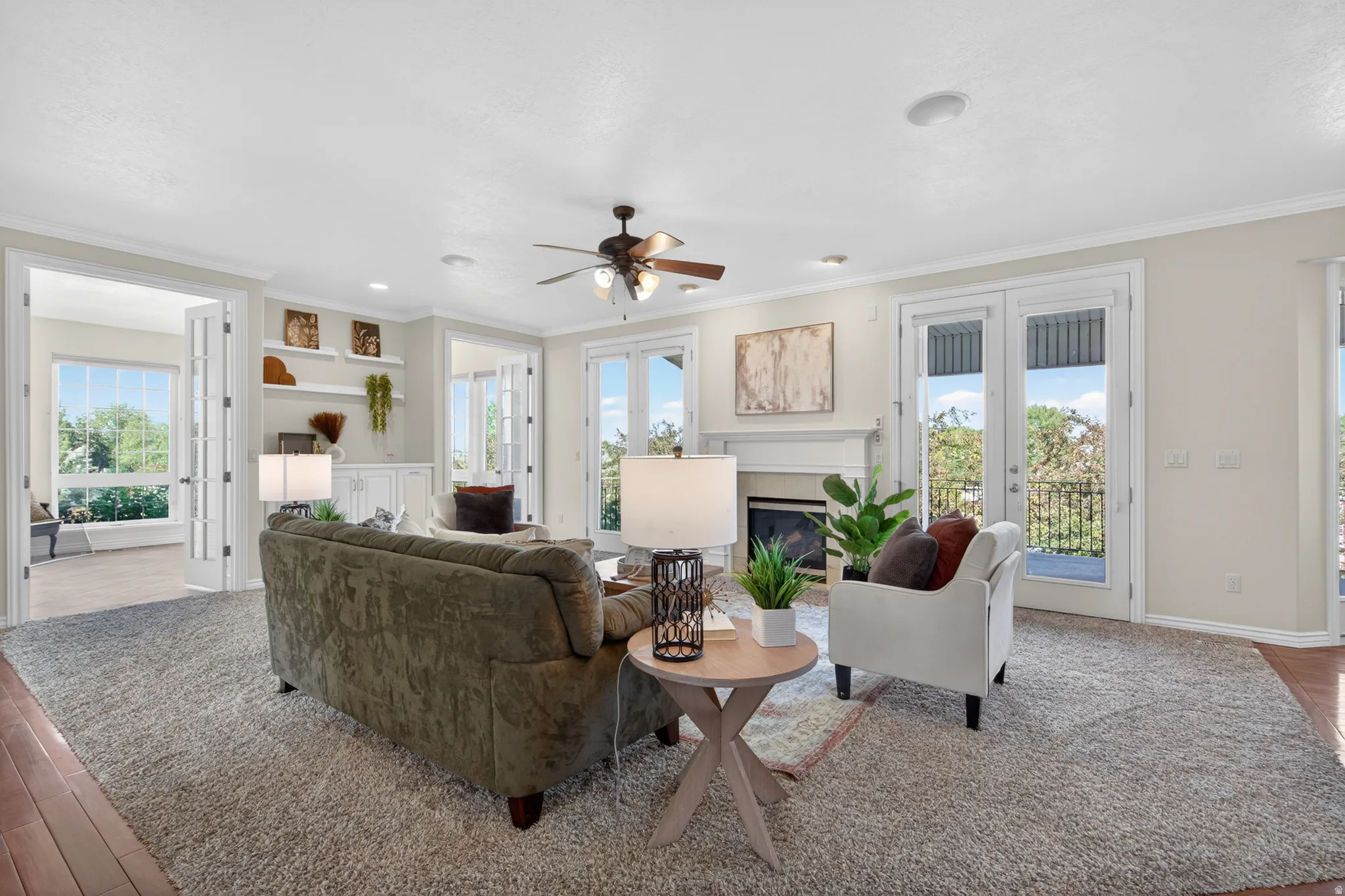 Spacious living area featuring a fireplace with a white mantel, hardwood-finish flooring, a ceiling fan, and multiple French doors providing exterior access