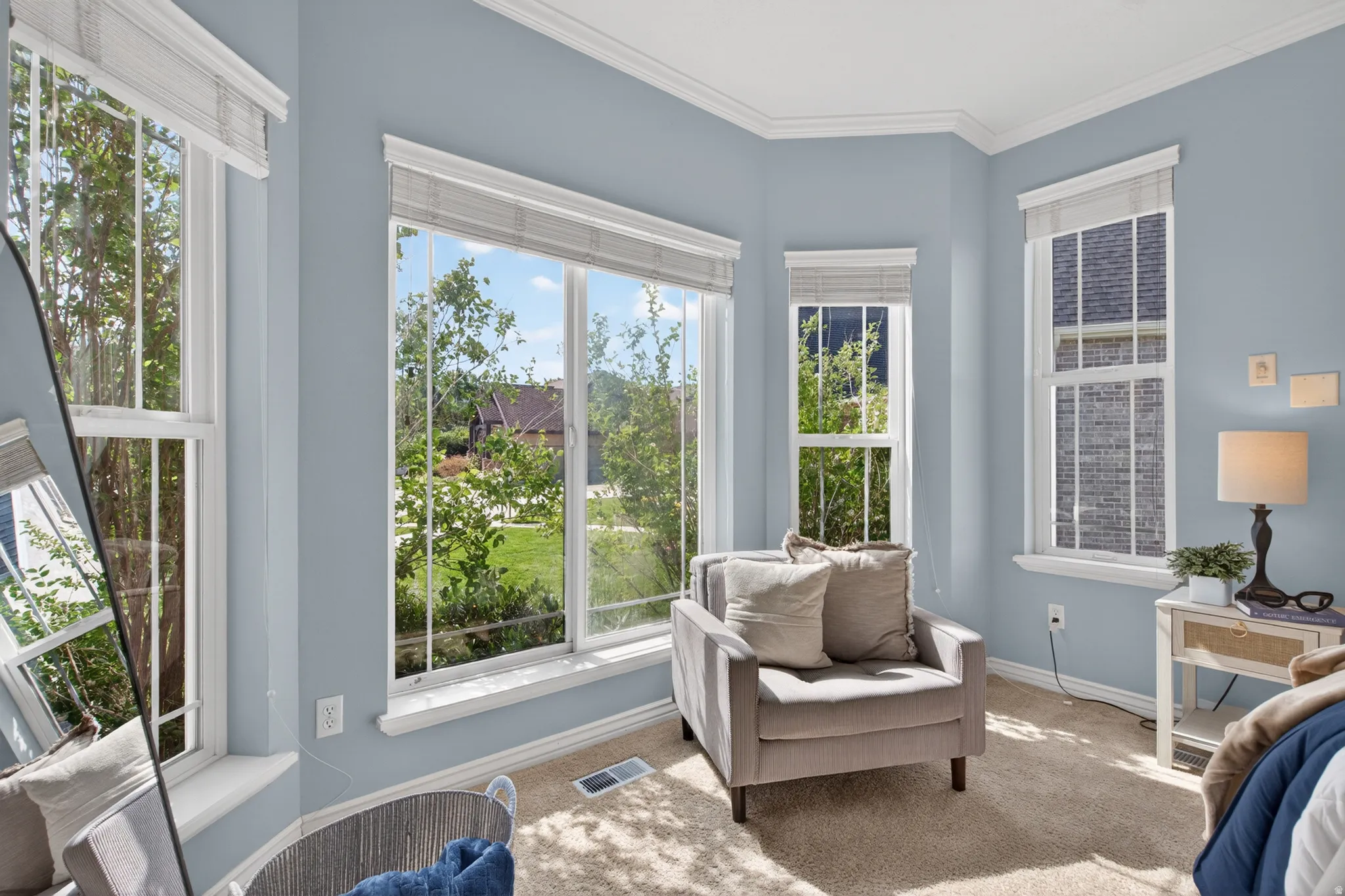 Bay window feature with multiple double-hung windows, crown molding, light blue wall paint, and beige carpet flooring