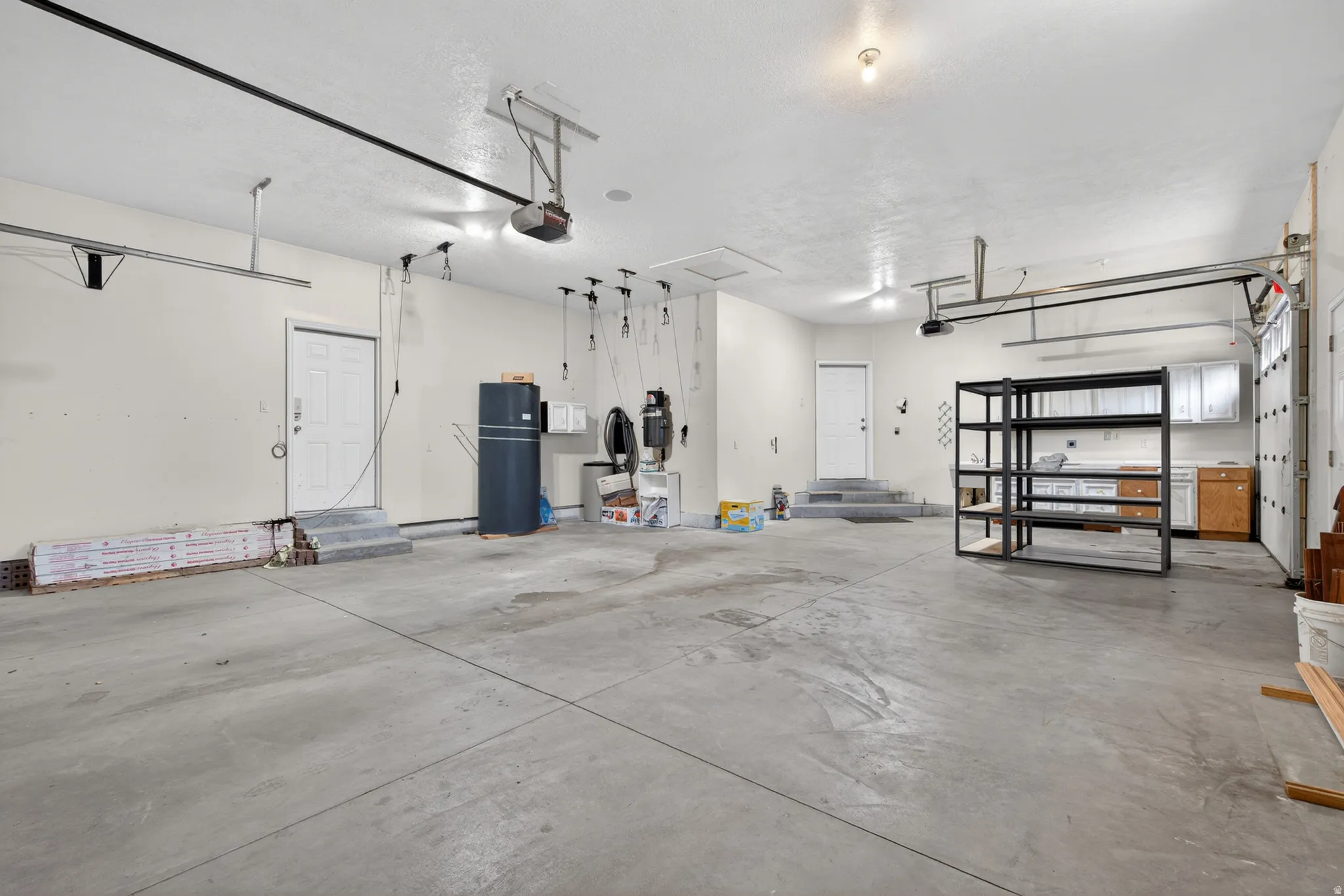 Spacious three-car garage featuring a concrete floor, bright overhead lighting, and built-in cabinetry with a countertop