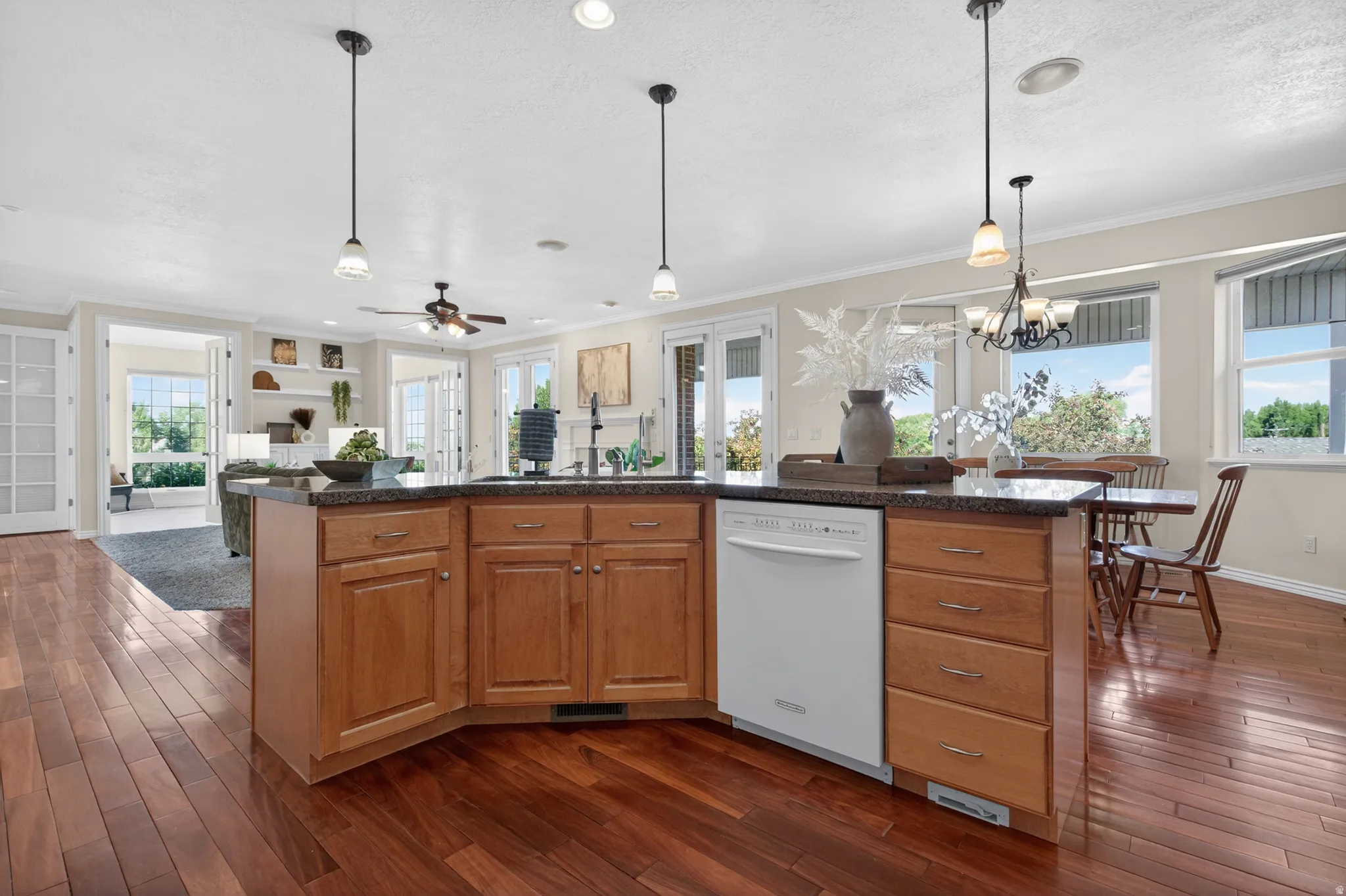 Kitchen island with wood cabinetry, dark countertop, and built-in dishwasher
