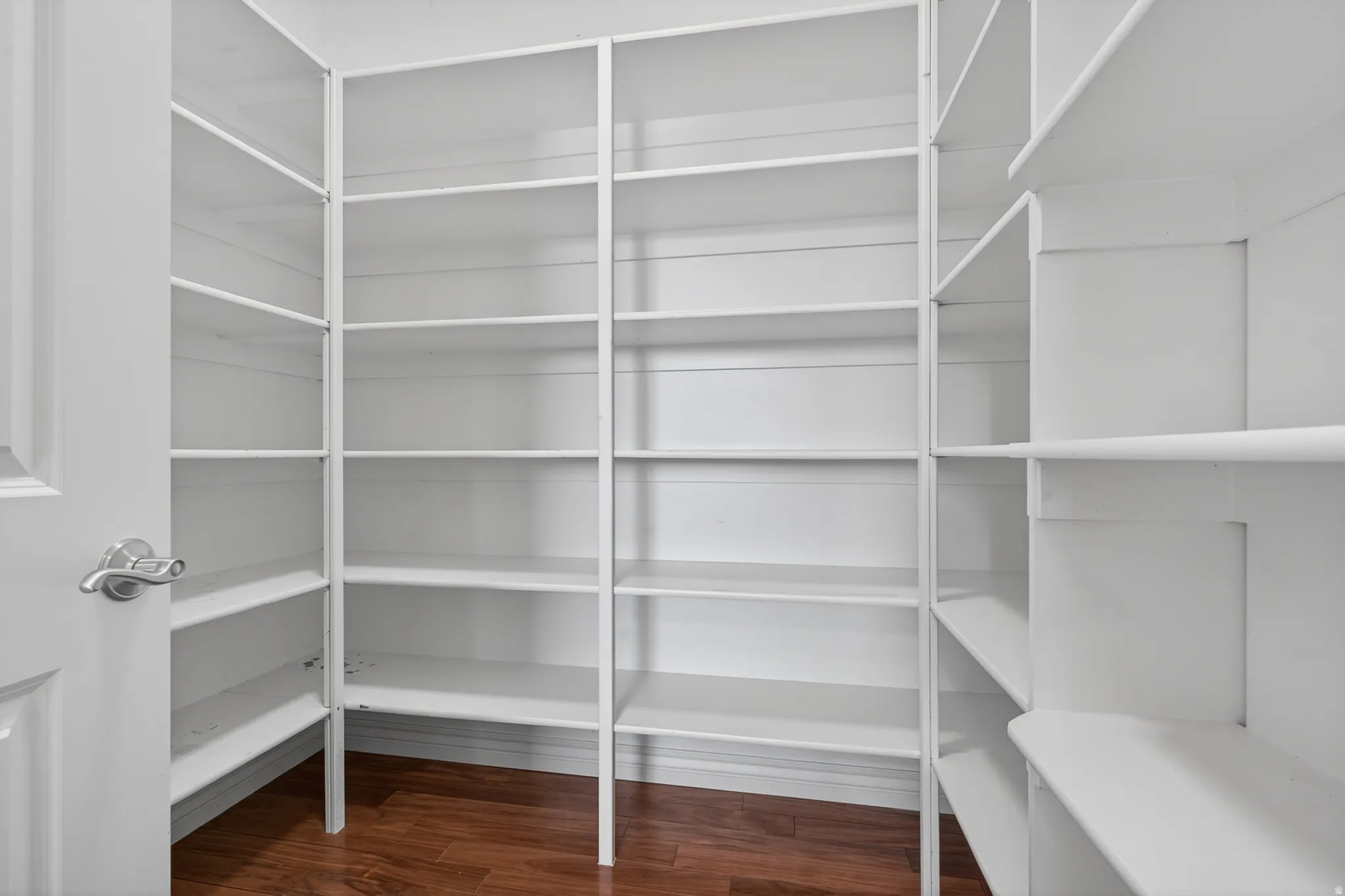 Walk-in pantry featuring extensive white shelving, multiple storage levels, and wood-finish flooring