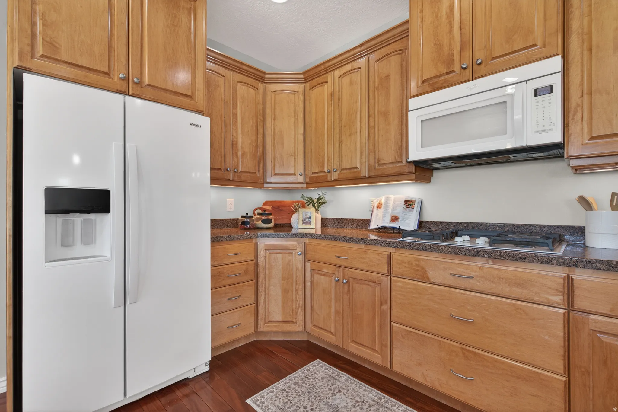 Kitchen featuring wood cabinetry, dark countertops, built-in microwave, and wood-finish flooring