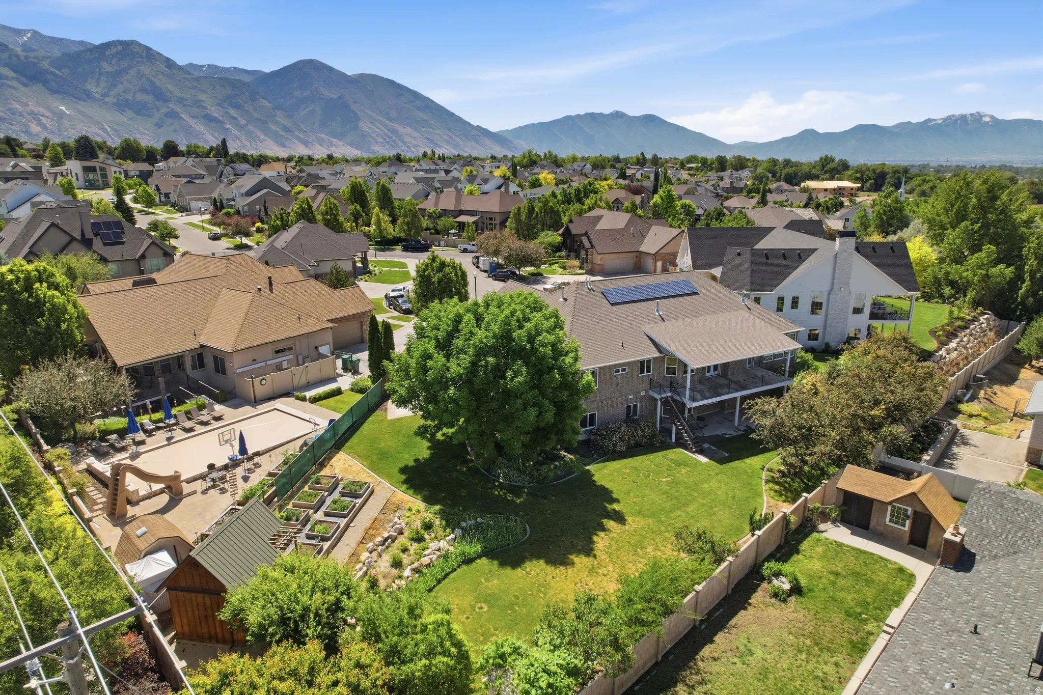 Expansive property featuring a meticulously landscaped backyard, multiple terraced garden beds, a large lawn area, and mature trees