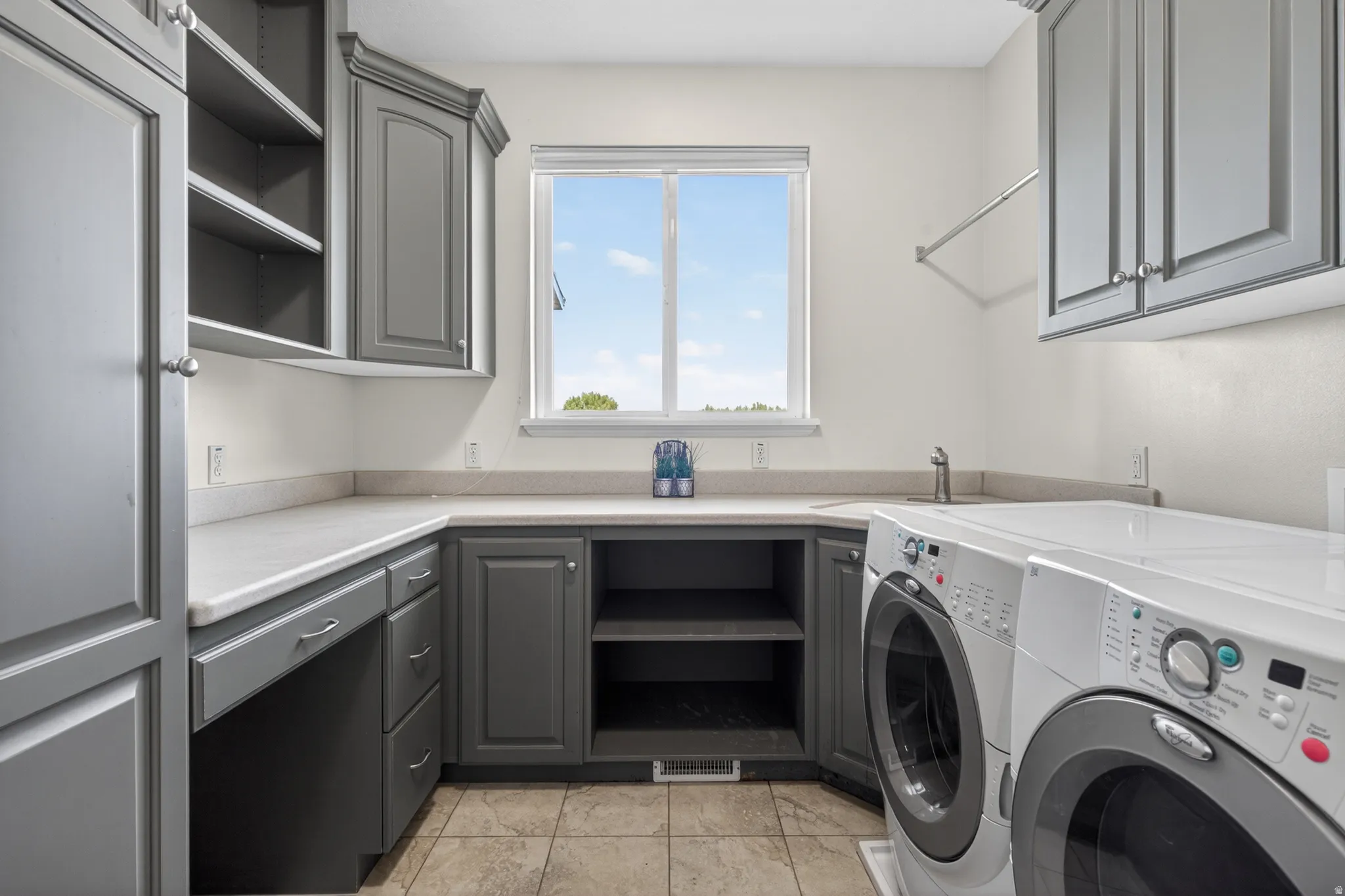 Laundry area featuring extensive grey cabinetry, light-toned countertops, and a window providing natural illumination