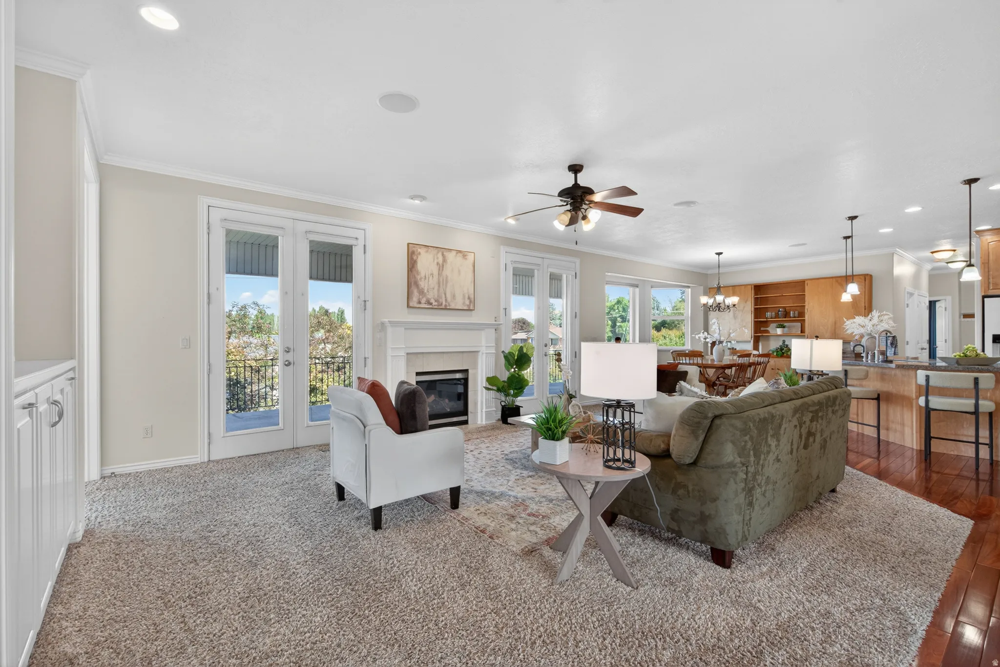 Spacious living area featuring a fireplace with a white mantel, dual French doors with balcony access, crown molding, and recessed lighting