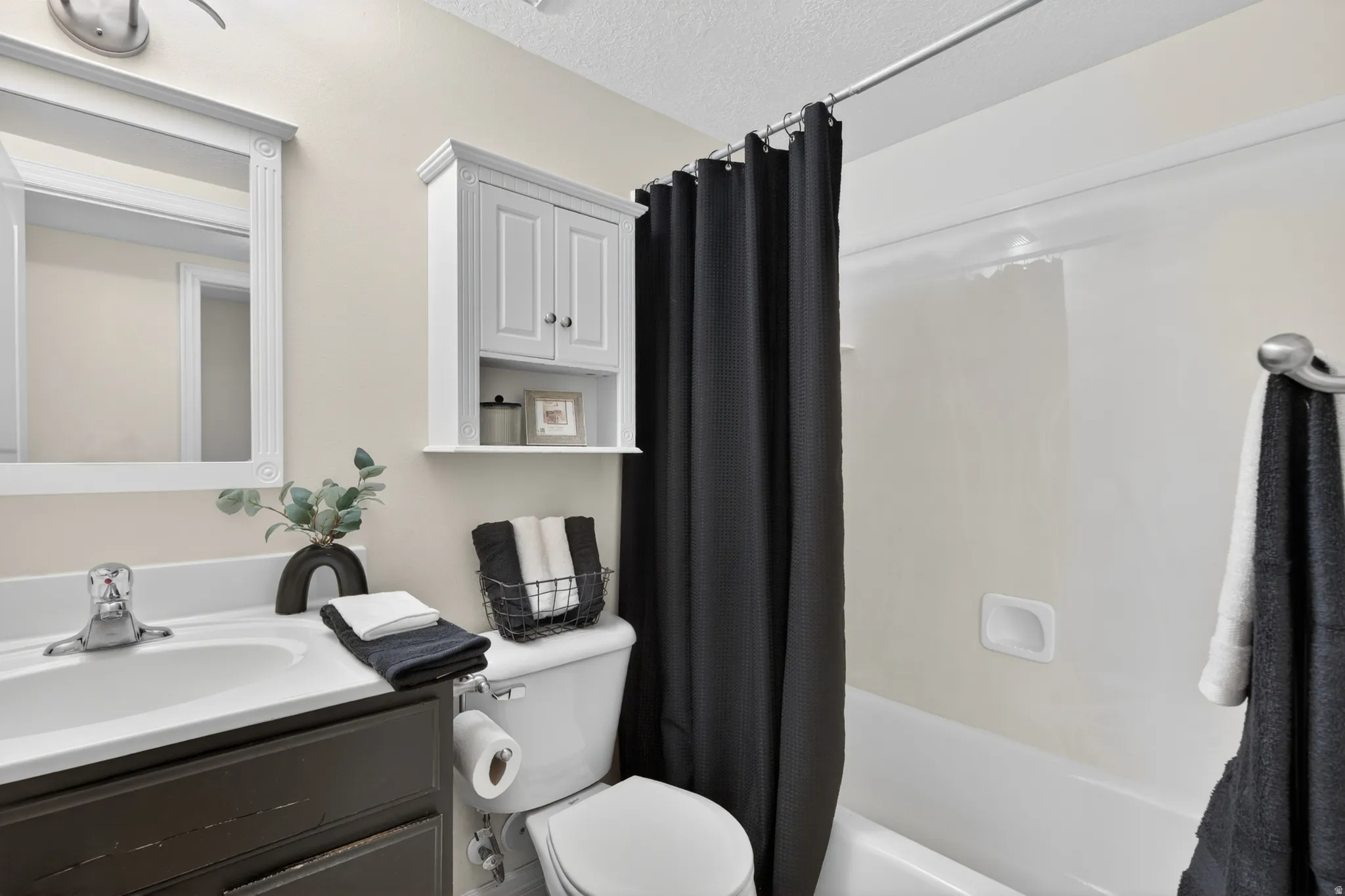 Bathroom featuring a tub/shower combination, white wall-mounted cabinet, vanity with dark wood-finish cabinetry, and a white framed mirror
