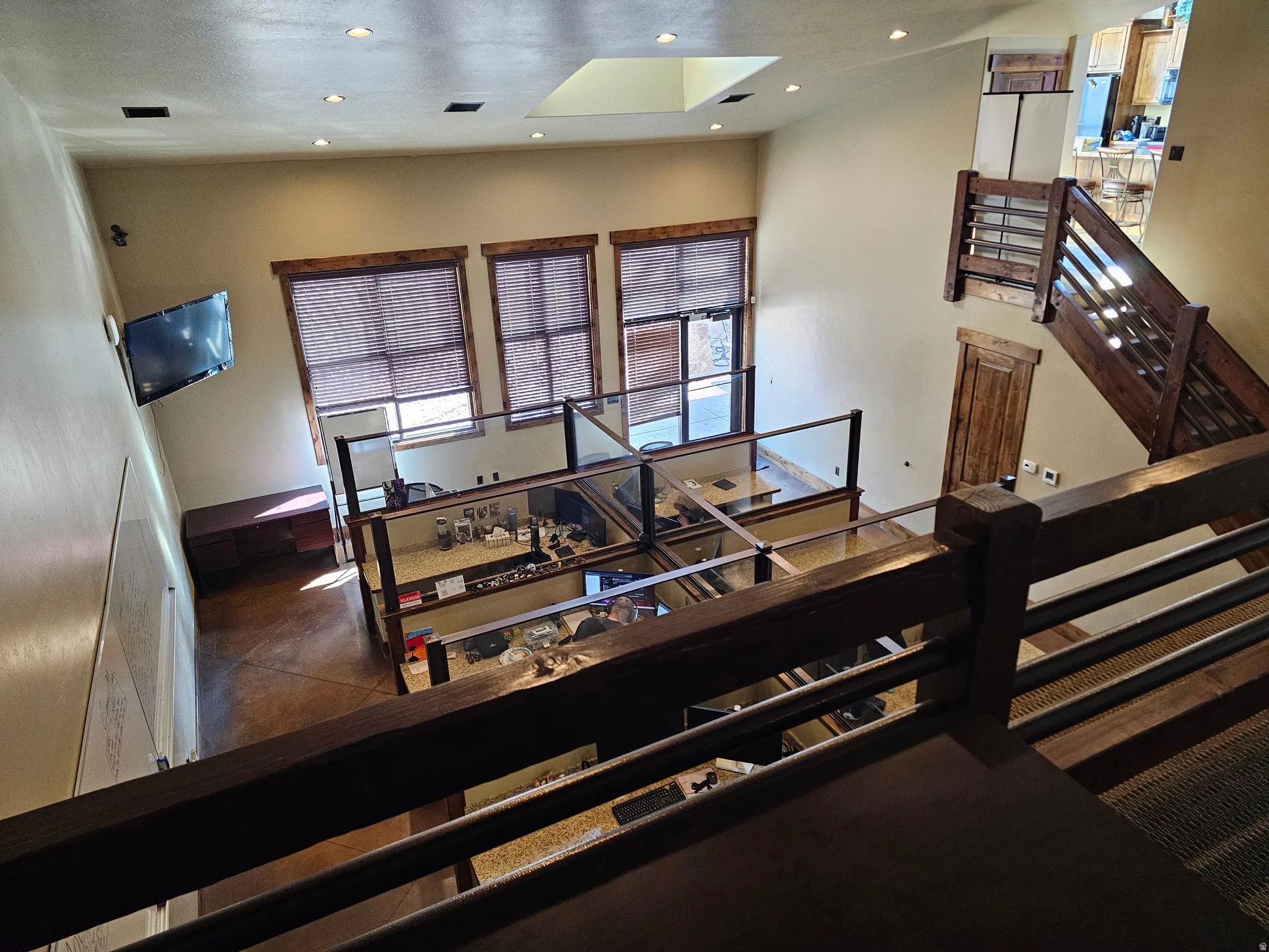 Open-concept multi-level interior featuring high ceilings, a skylight, three large windows with wood-finish blinds, and a prominent wood-and-metal staircase