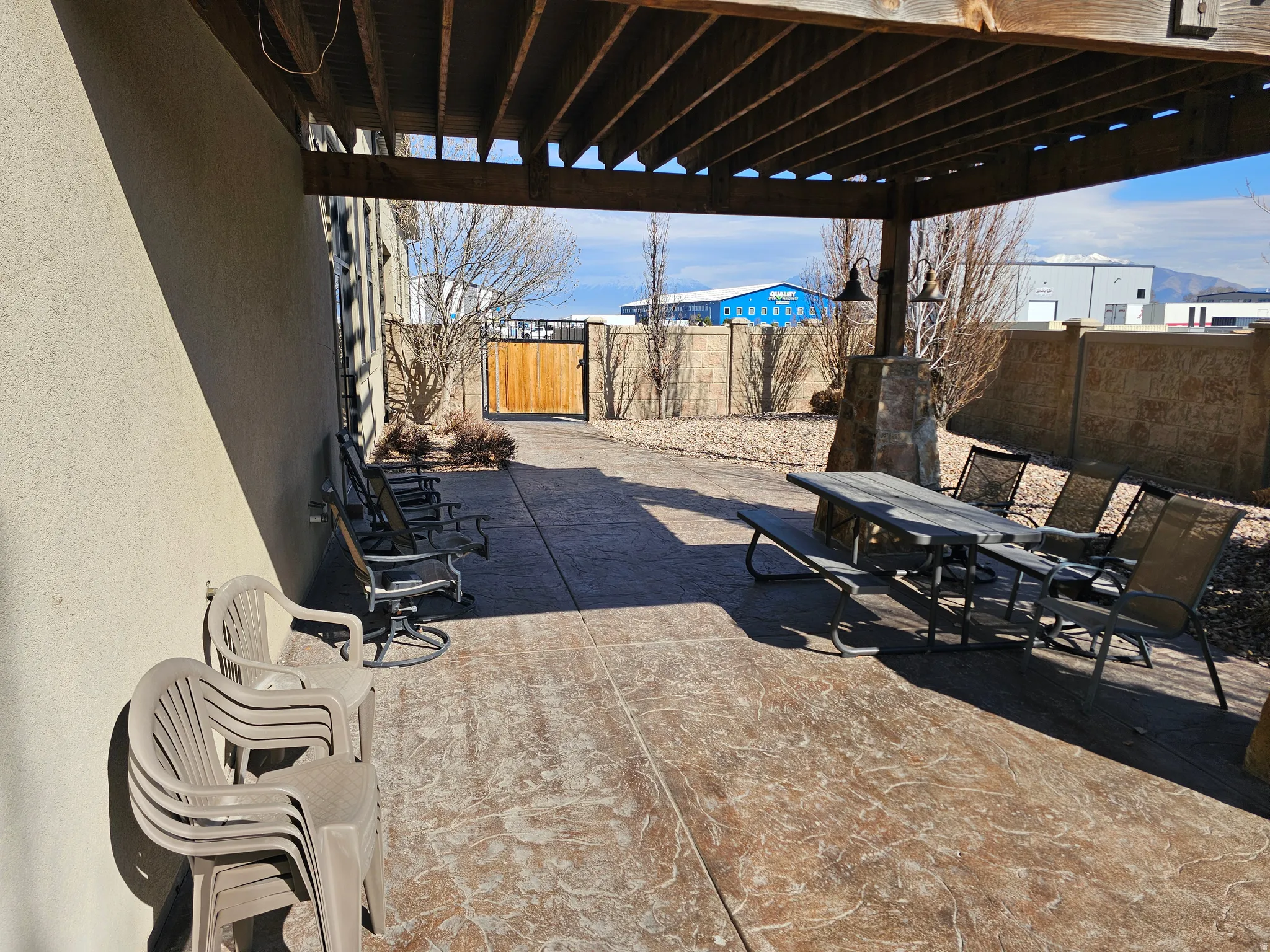 Expansive stamped concrete patio featuring a wooden pergola, stone-clad pillar with integrated lighting, and a private wooden gate