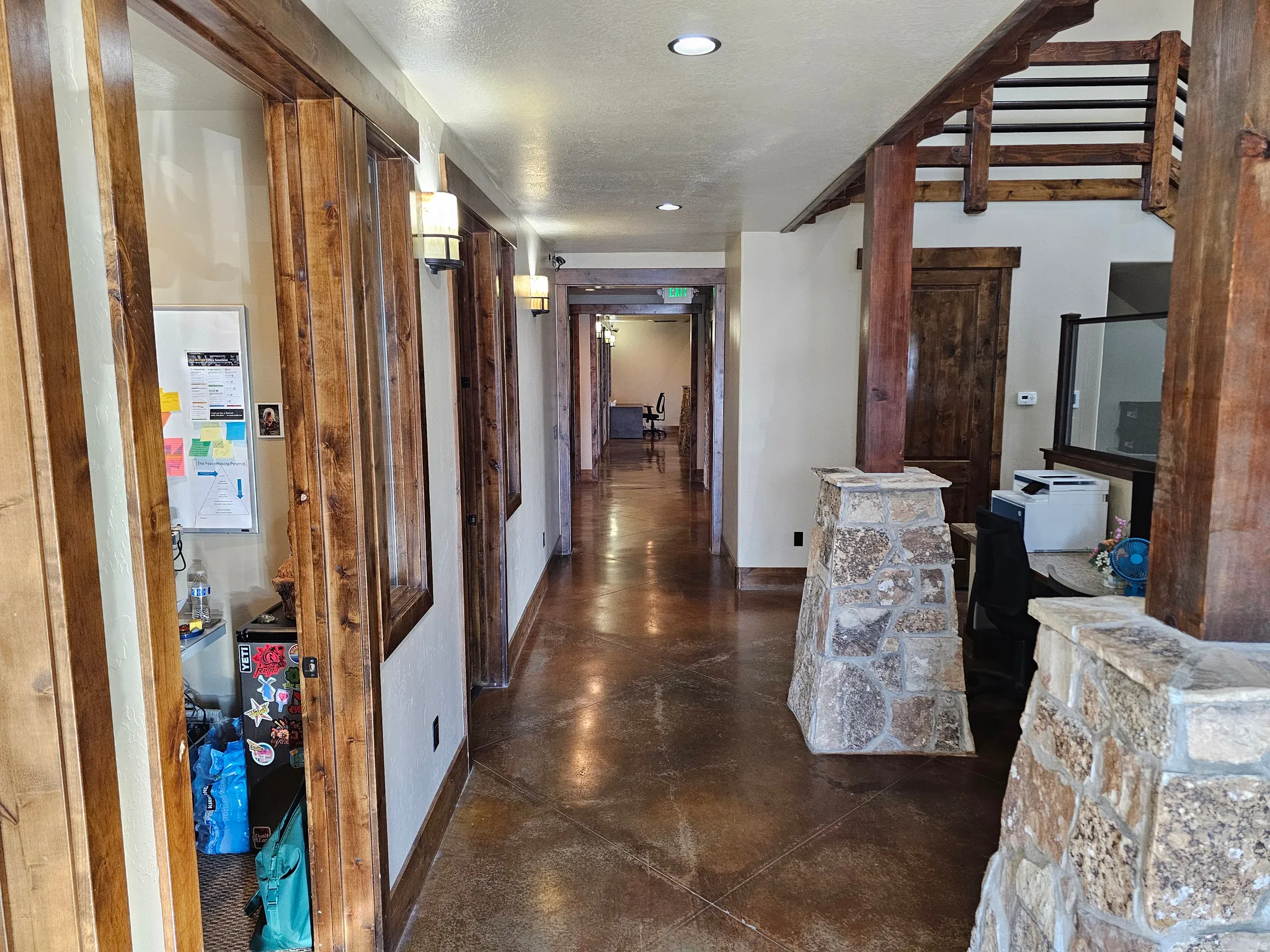 Hallway featuring wood-finish flooring, stone-clad pillars, exposed wood beams, and multiple wall sconces
