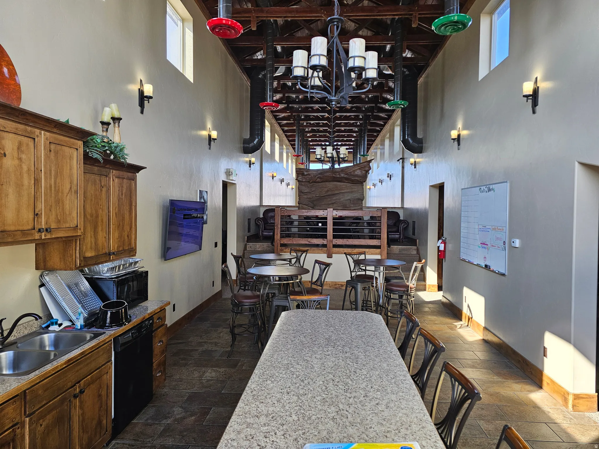 Spacious common area featuring an exposed beam ceiling, wall sconces, clerestory windows, and a built-in kitchenette with wood cabinetry and a double basin sink