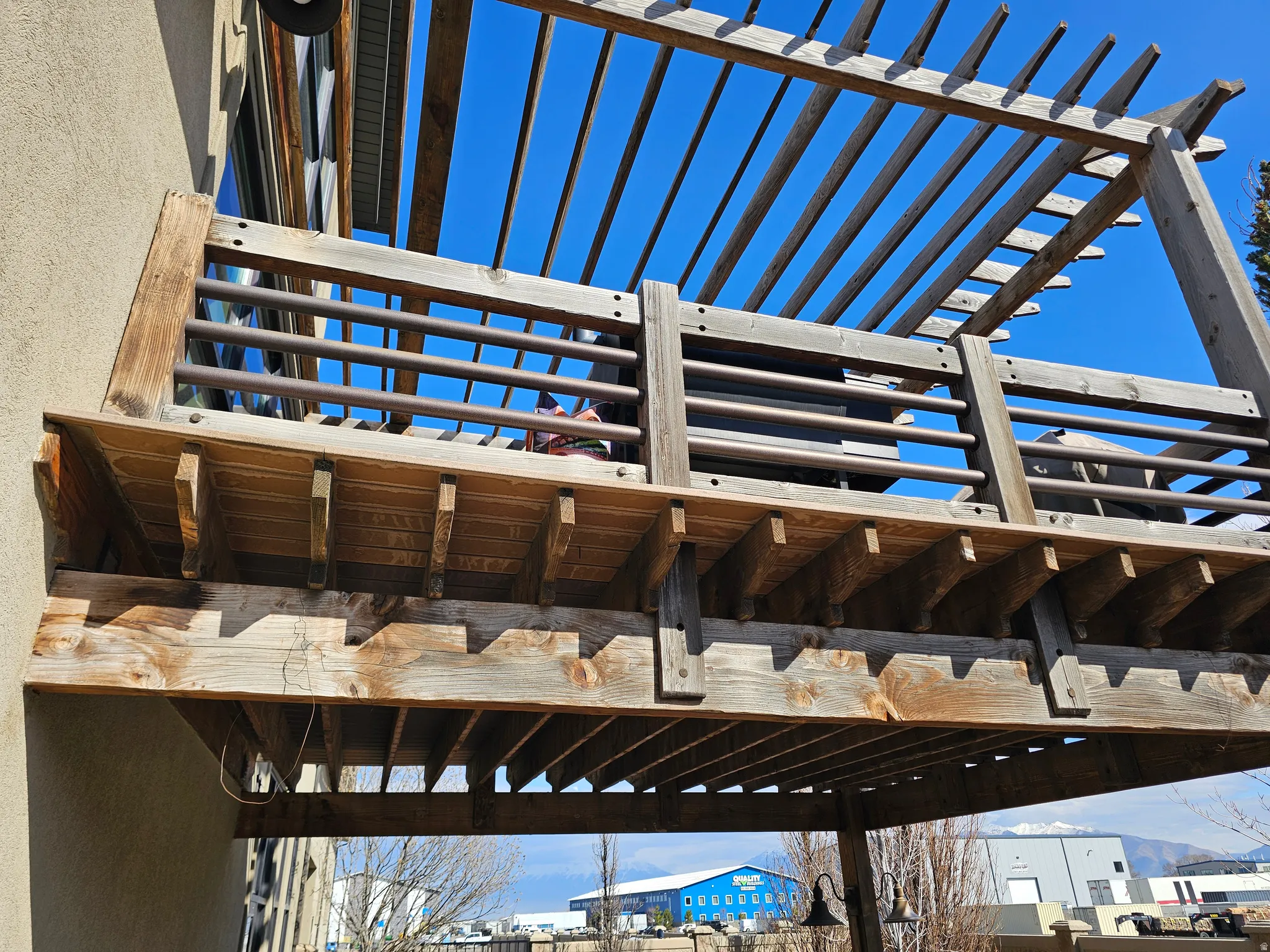 Upper-level wooden deck featuring a slatted pergola overhead and horizontal metal railings
