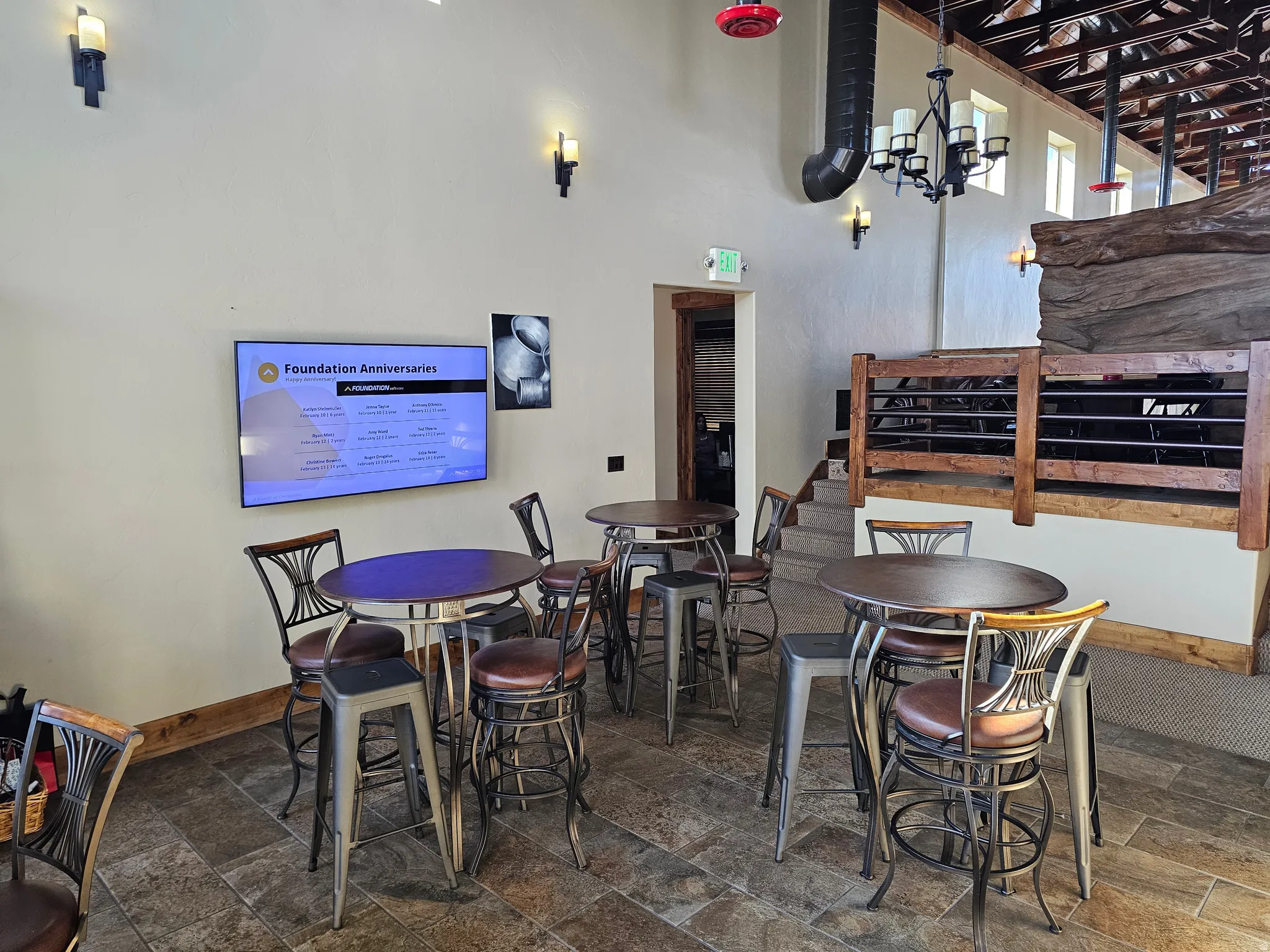 Spacious interior featuring a stone-look tile floor, exposed ceiling beams, and a built-in staircase with a wood and metal railing