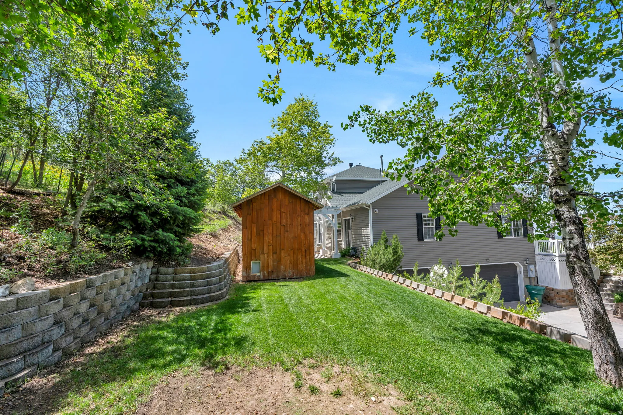 Expansive lawn with mature trees and a wooden storage shed