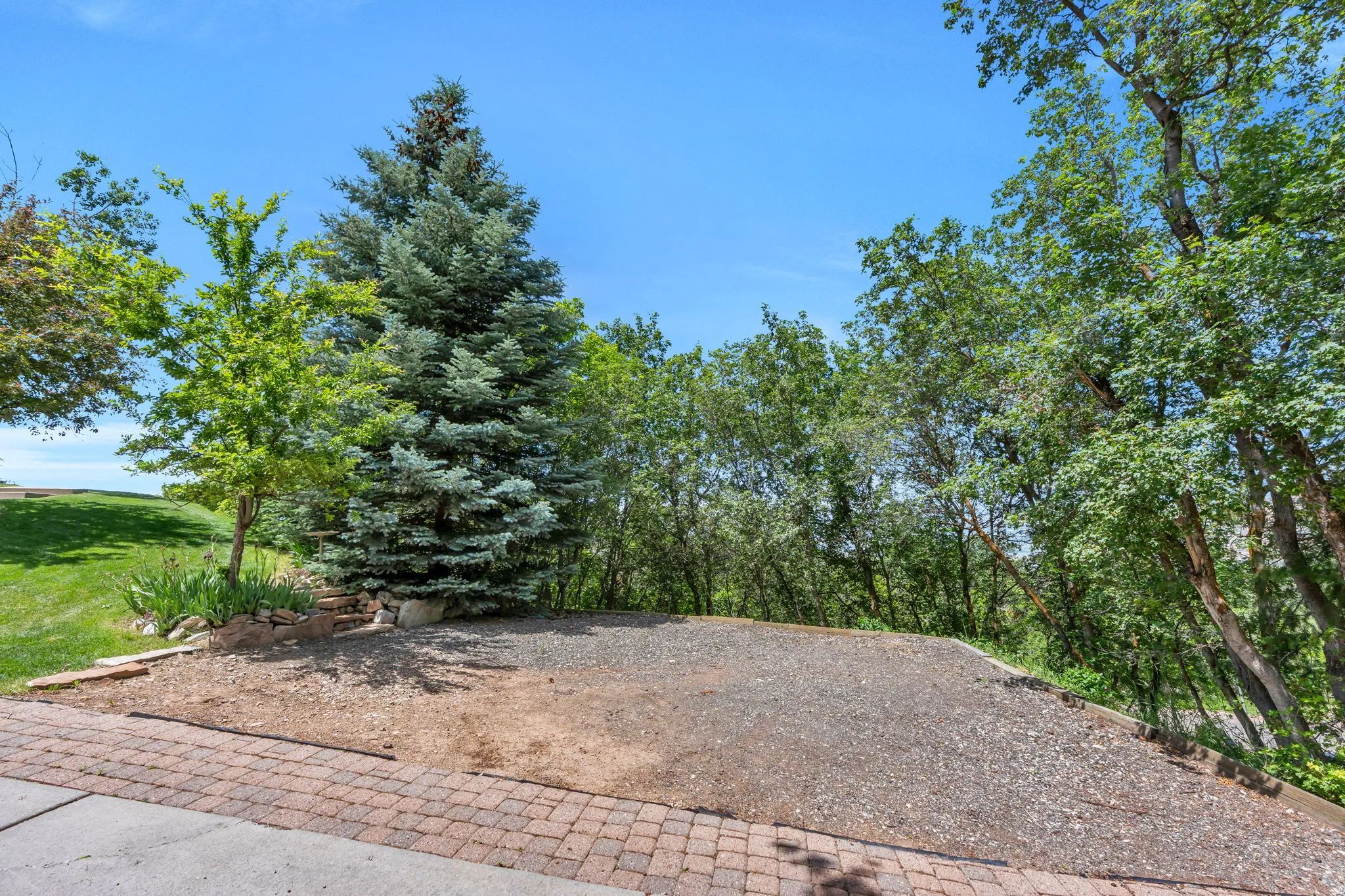 Gravel area bordered by a paver stone edge, surrounded by mature trees and a manicured lawn