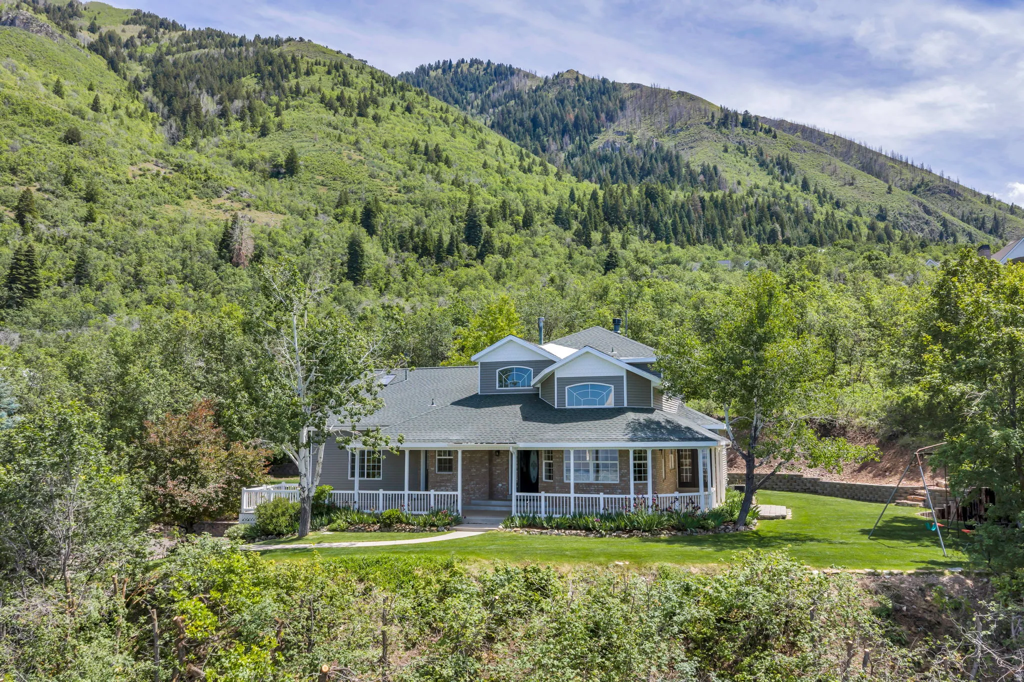 Expansive property featuring a multi-level home with a wrap-around porch, dormer windows, and a manicured lawn