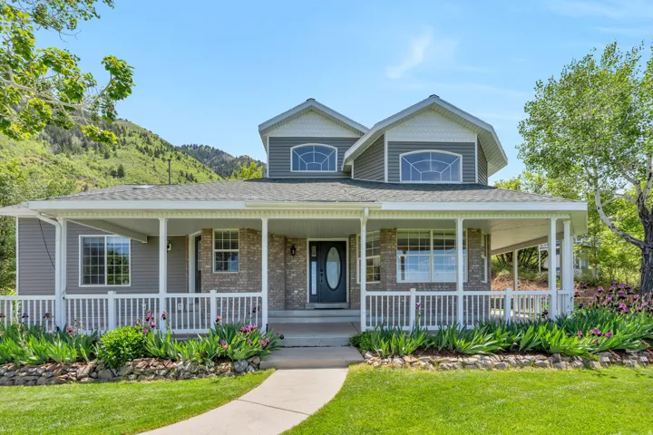 Two-story home featuring a broad covered front porch with white railing, stone accents, and dark siding