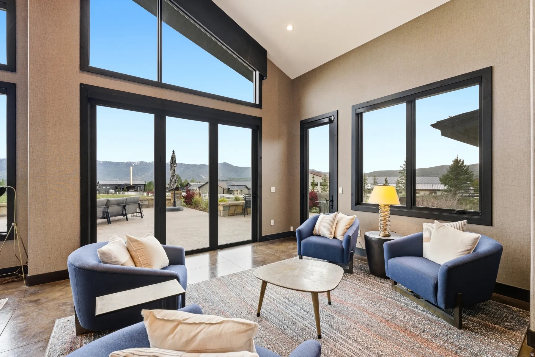 Vaulted ceiling living space with large black-framed windows and a multi-panel glass door to the exterior patio