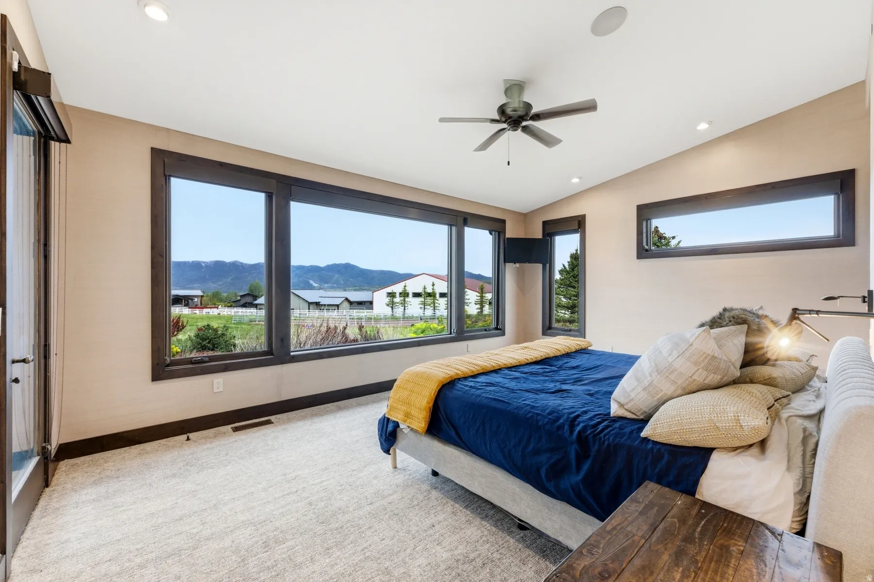 Spacious room featuring a wall of expansive windows with dark wood trim, light beige walls, recessed lighting, and a ceiling fan