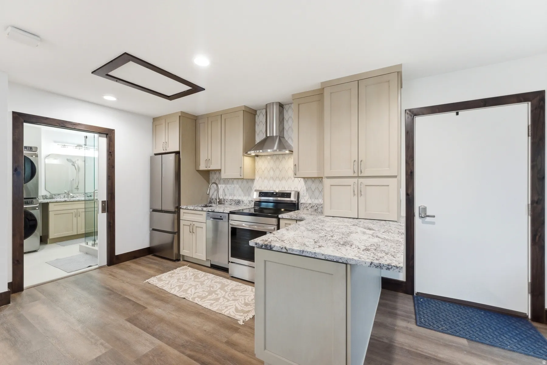 Kitchen featuring light-toned cabinetry, stainless steel appliances, a stone countertop island, and wood-finish flooring