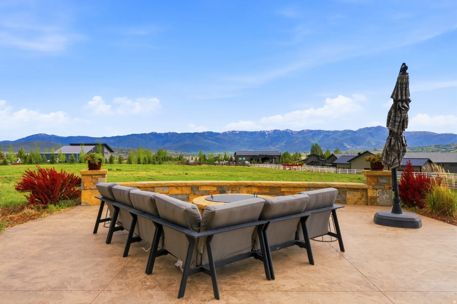Expansive stamped concrete patio featuring a built-in stone fire pit and a stone retaining wall