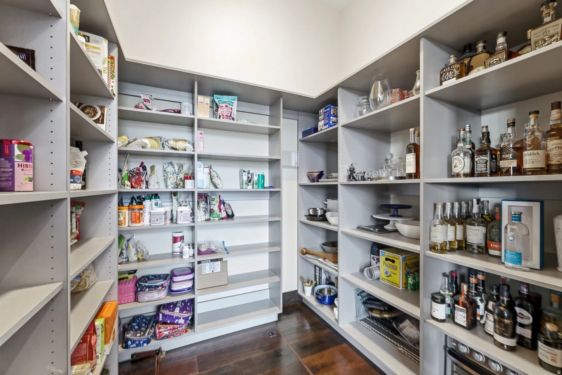Spacious walk-in pantry featuring extensive built-in shelving, dark wood-finish flooring, and ample storage capacity