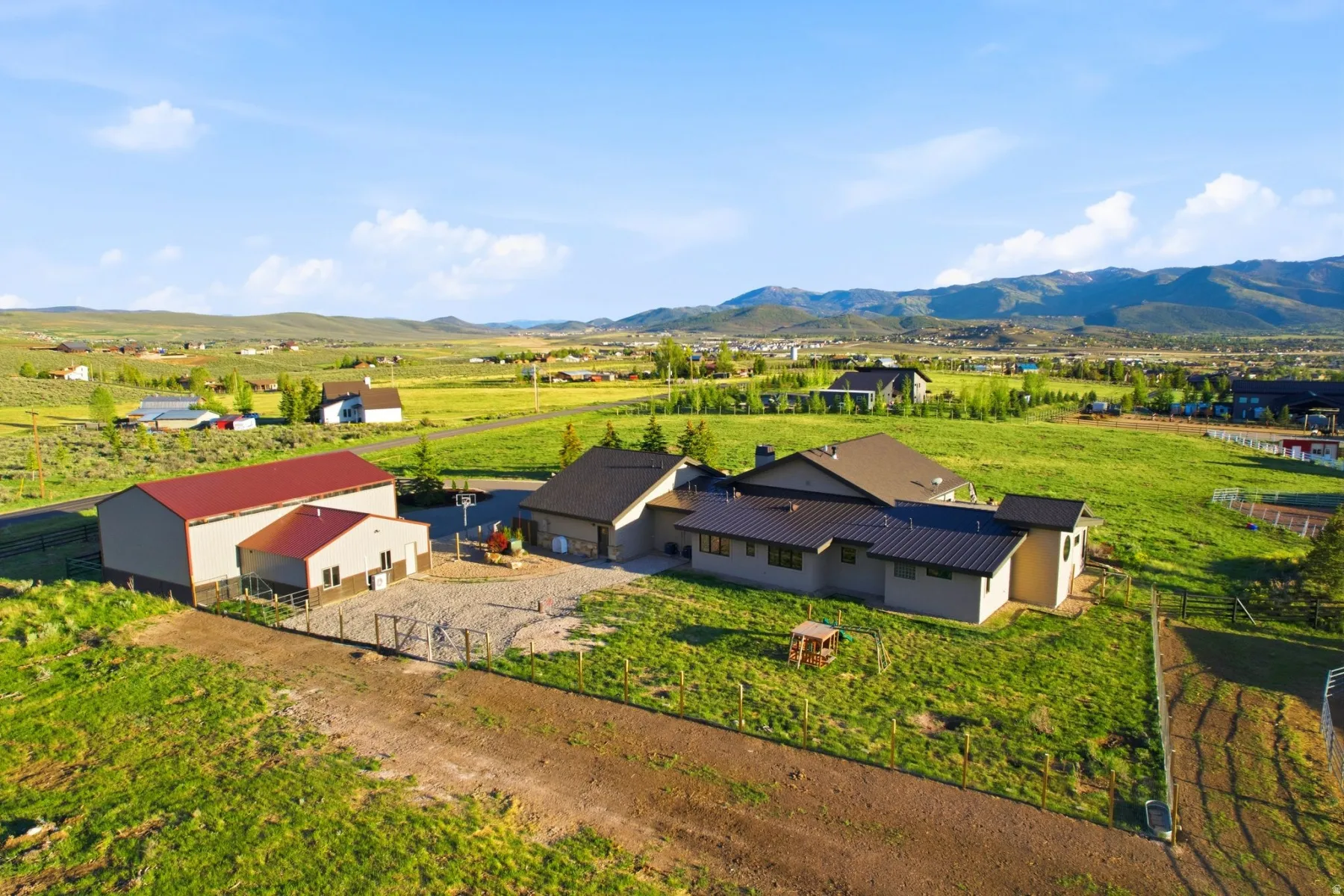 Expansive property featuring a contemporary residence with a metal roof, a large outbuilding with a red metal roof, and a separate structure with a matching red metal roof
