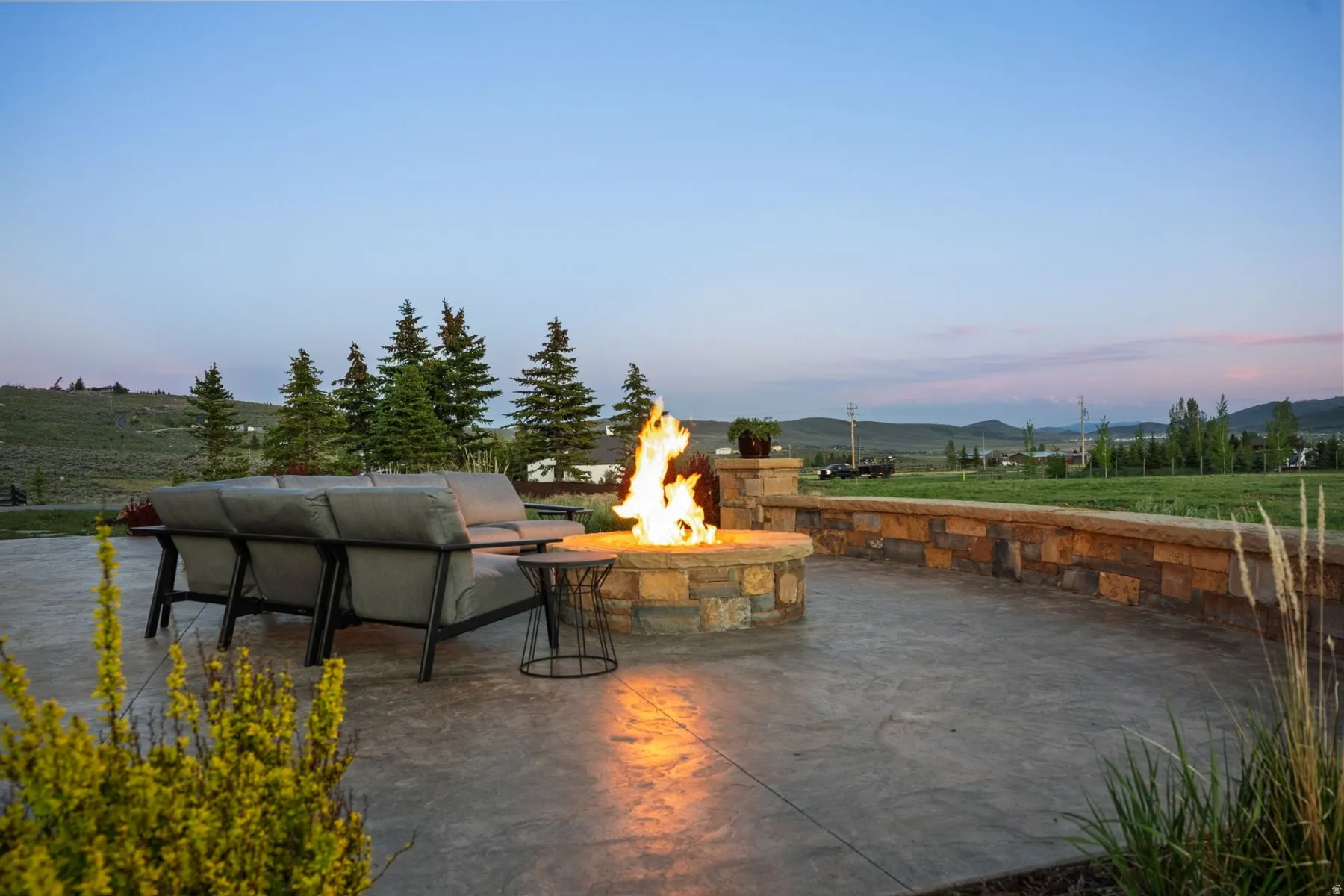 Expansive outdoor patio featuring a stone fire pit, stamped concrete flooring, and a stone retaining wall
