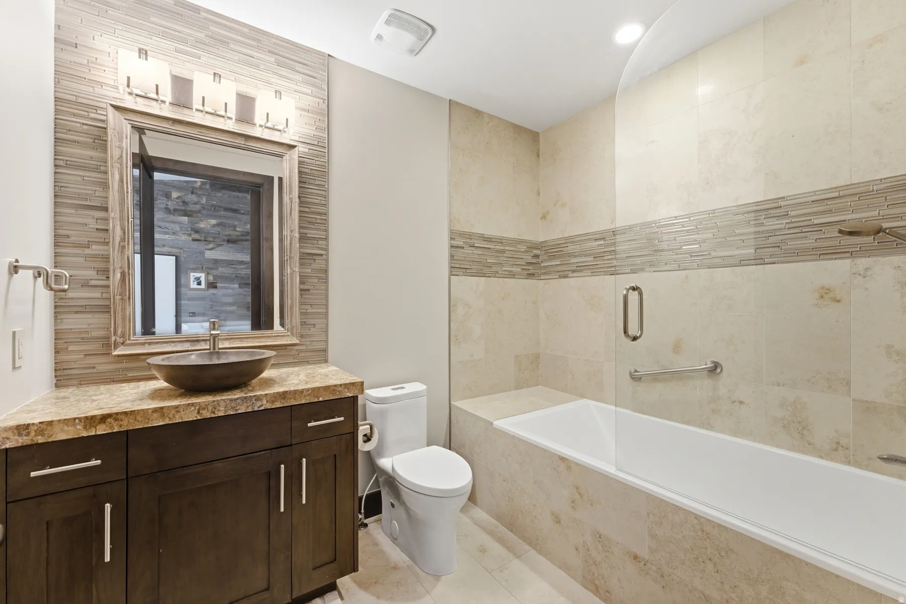Bathroom featuring a vessel sink with a dark wood-finish vanity, a framed mirror, and a tiled shower/tub combination with a glass panel