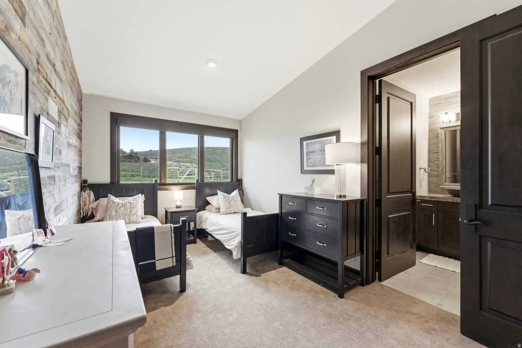 Bedroom featuring a reclaimed wood accent wall, broad windows framing a rural landscape, and plush carpet flooring