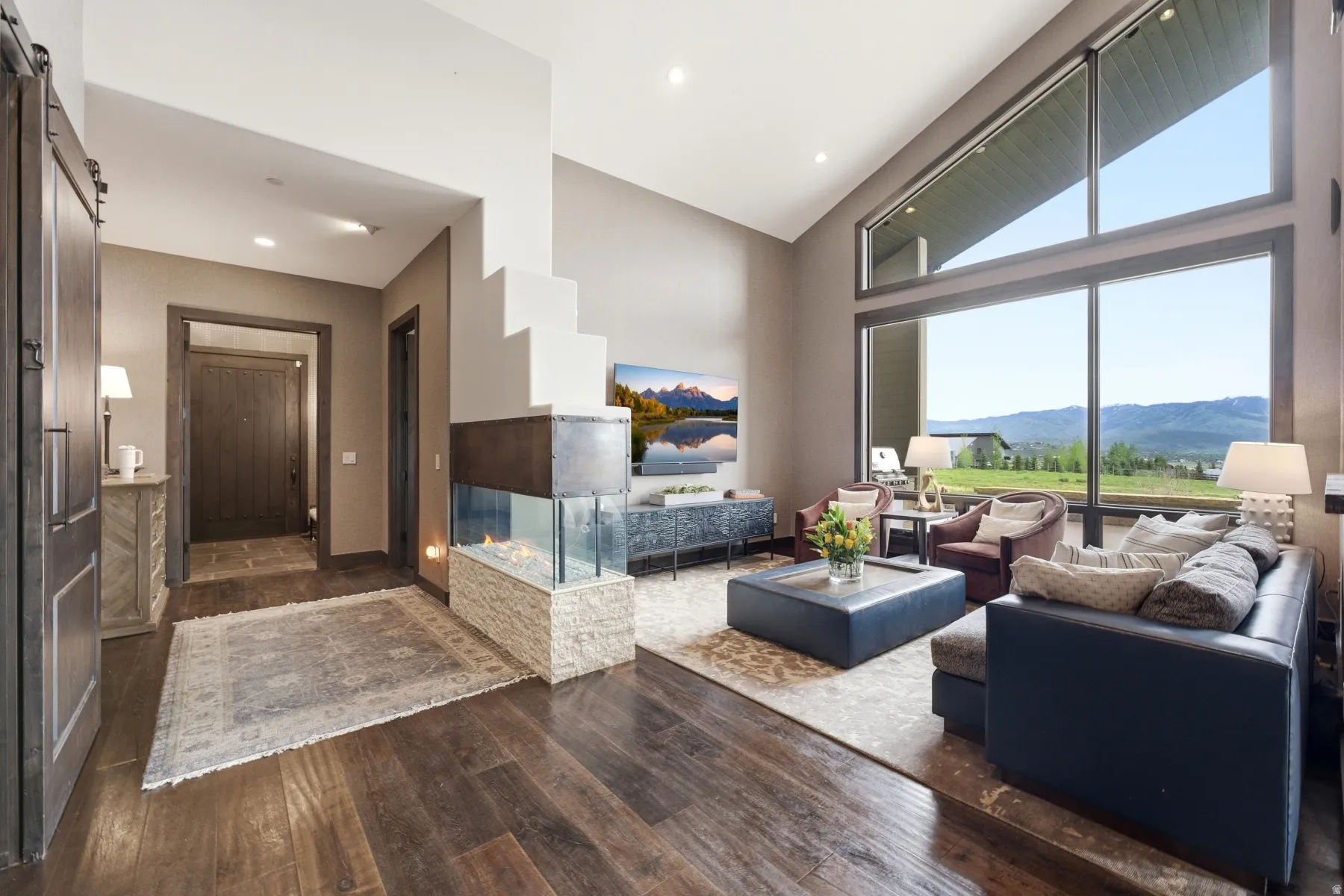 Spacious living area featuring expansive windows, vaulted ceilings, and dark wood-finish flooring