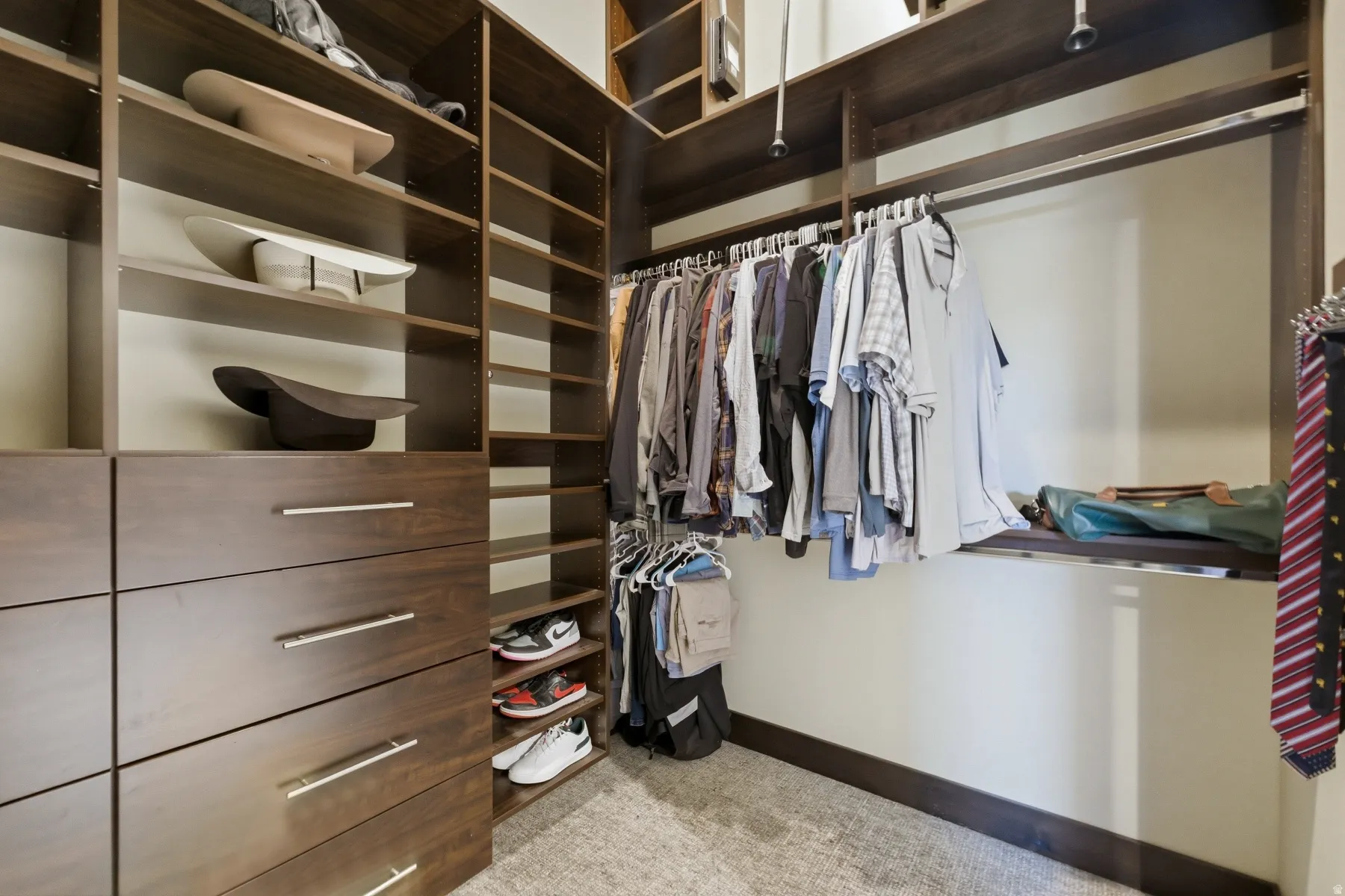 Custom closet system featuring dark wood-finish cabinetry, built-in shelving, multiple hanging rods, integrated drawers with brushed nickel hardware, and dedicated shoe storage