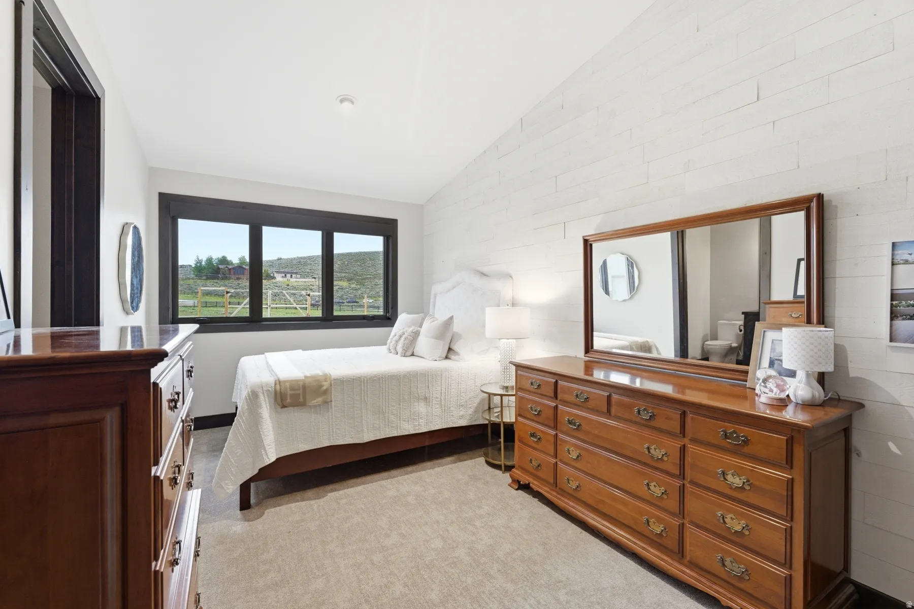 Bedroom with a large black-framed window, light-colored plank wall accent, dark wood-finish door casing, and neutral-toned carpeting