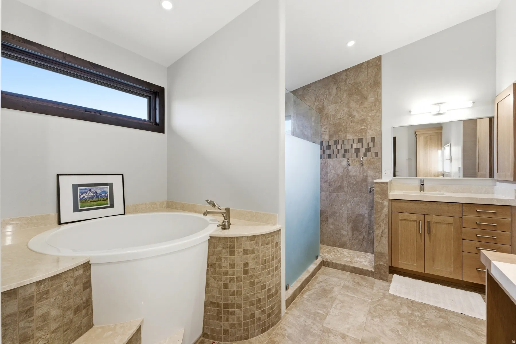 Built-in soaking tub with a tiled surround, complemented by a walk-in shower featuring a frosted glass panel and stone-finish tile