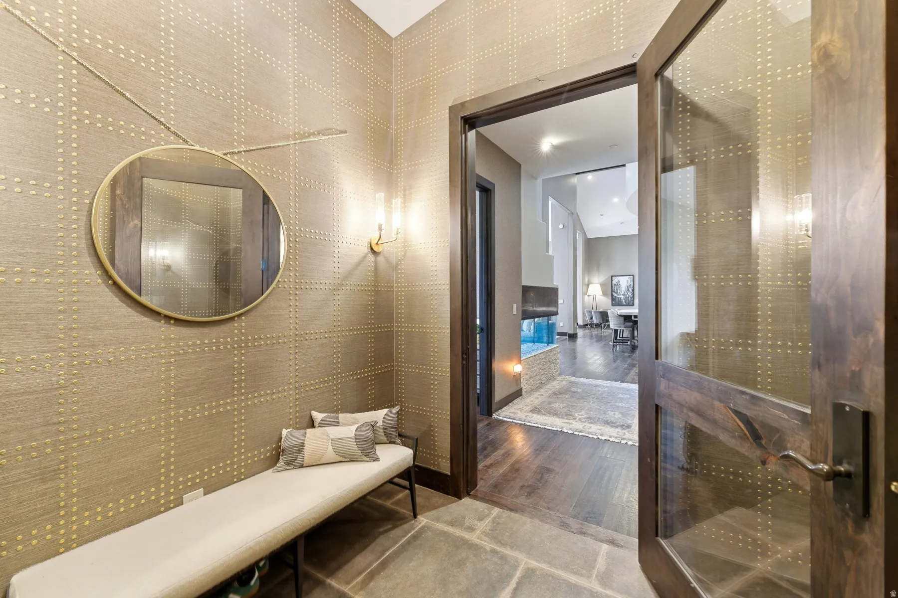 Entryway featuring patterned wall covering with metallic accents, a round wall-mounted mirror, and stone flooring